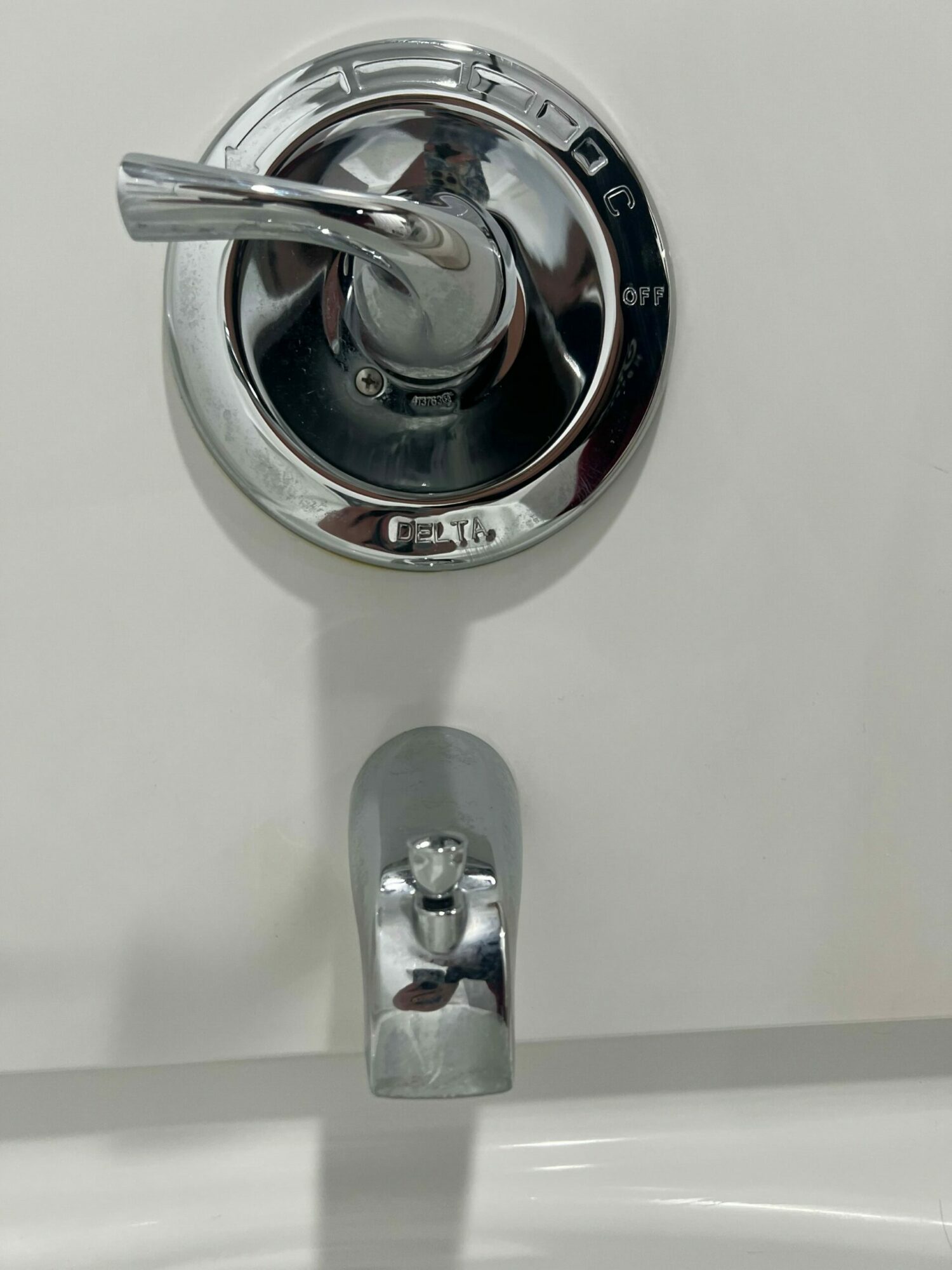 Close-up of a chrome faucet handle and a small cylindrical fixture on a white surface.