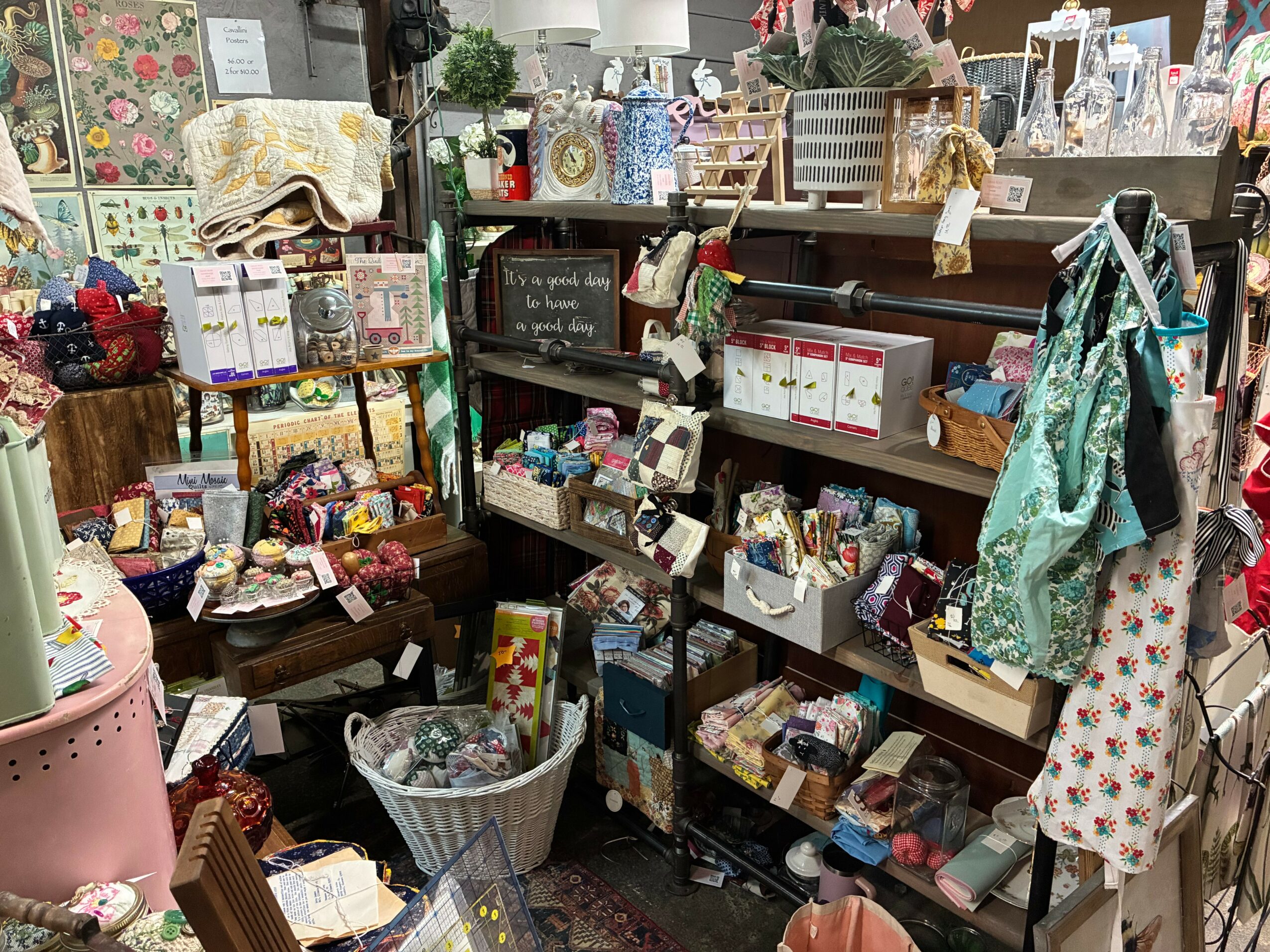 A cluttered display of various craft supplies, fabrics, and decorative items on shelves and tables in a store.