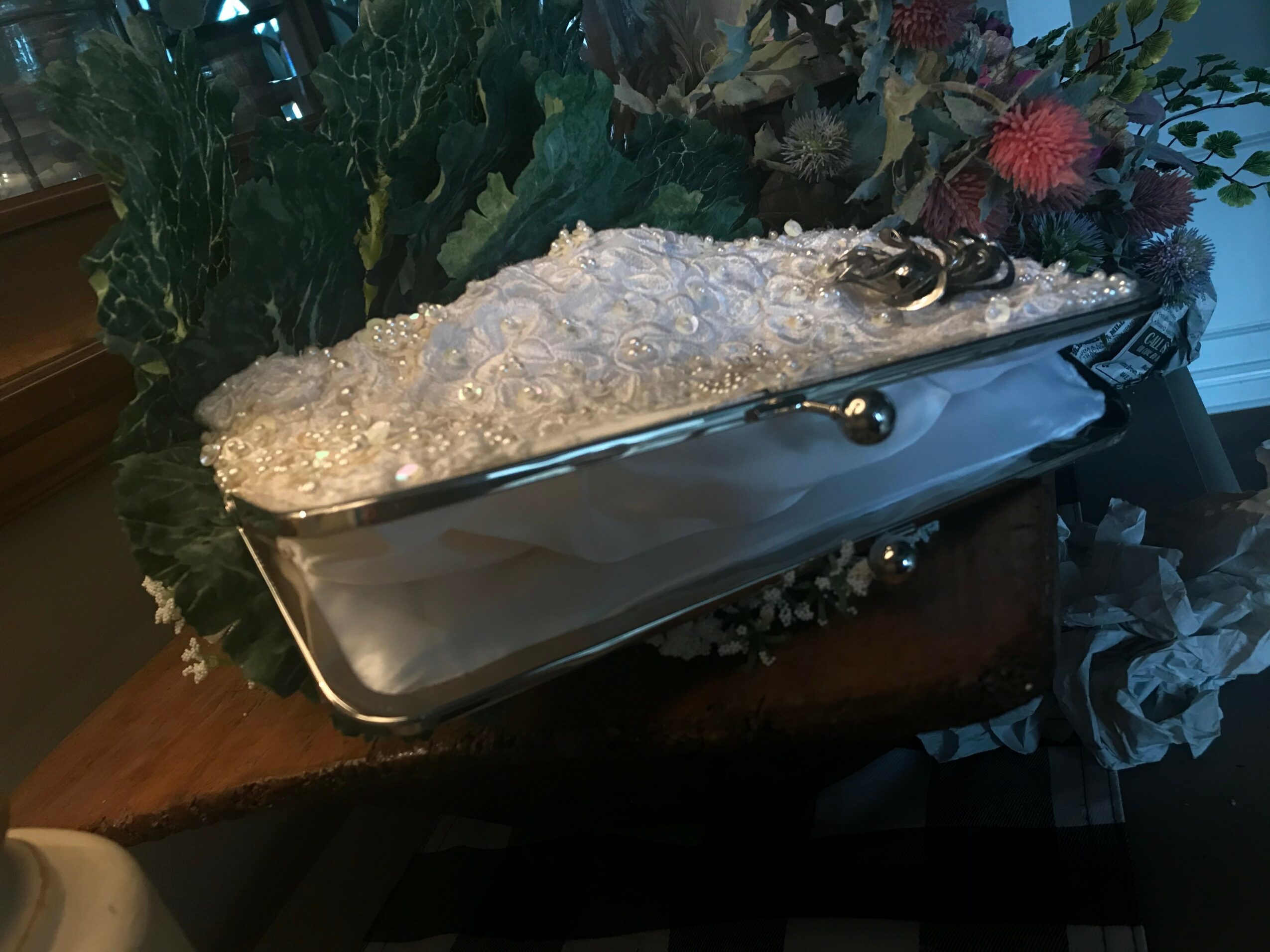 A silver tray with a floral arrangement and decorative items, placed on a wooden surface with plants and flowers in the background.