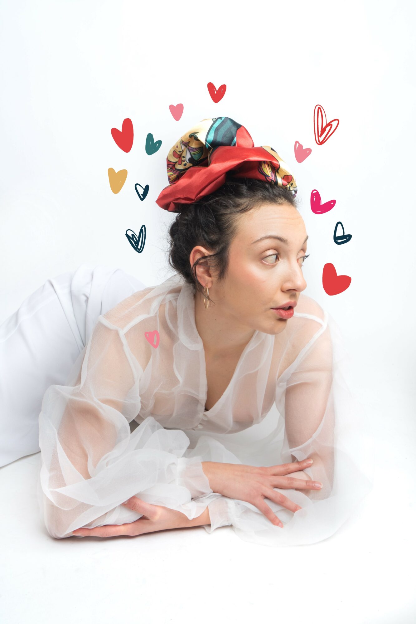 Woman lying on her side with colorful hearts and doodles above her head, wearing a sheer white top and a headscarf.