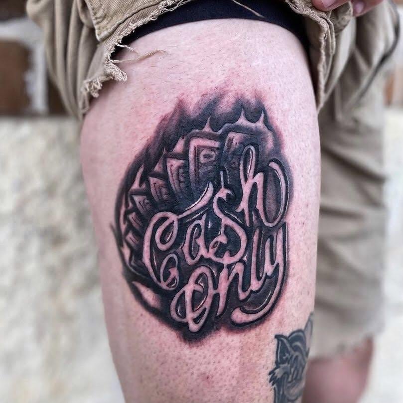 Tattoo of a burning dollar bill with the words 'Cash Only' in stylized script on person's thigh.