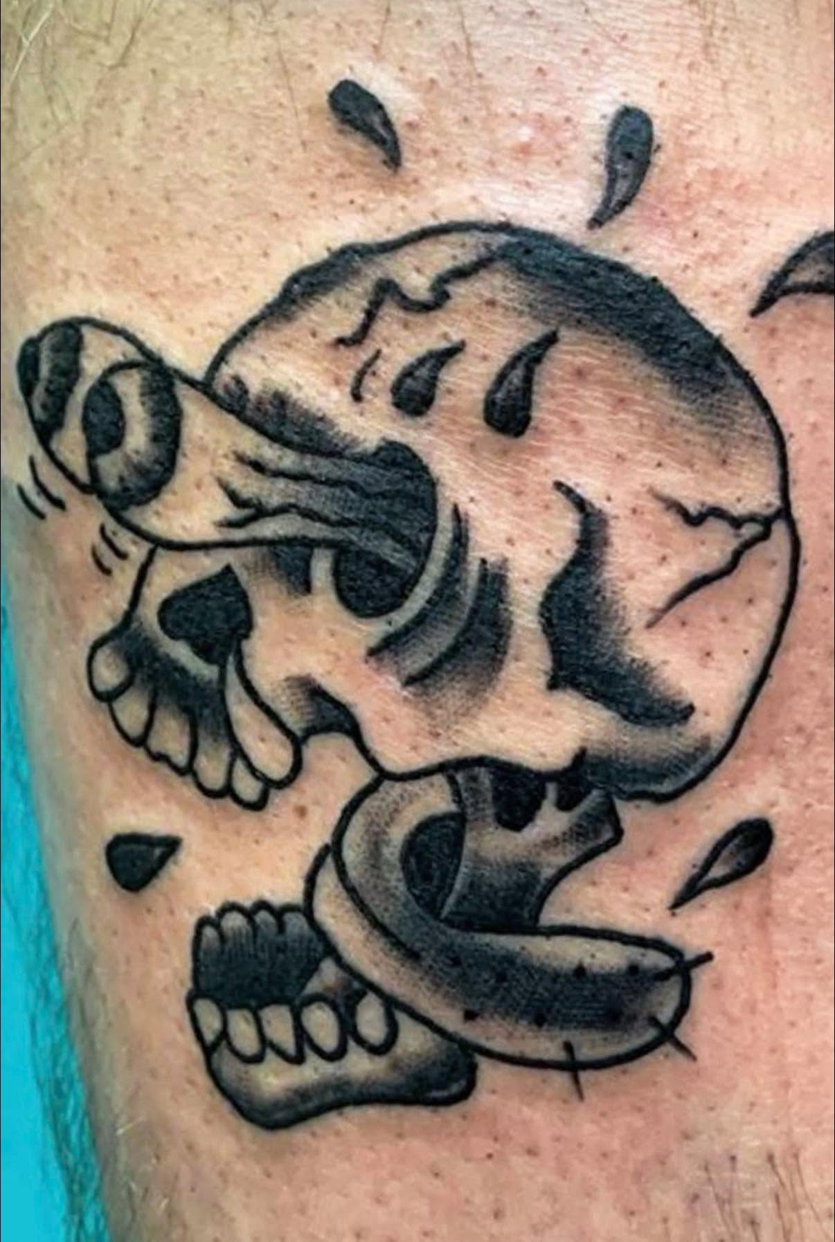 Tattoo of a skull with a snake wrapped around it, and a butterfly near the skull's eye socket.