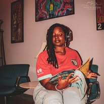 Woman with headphones reading a book in a room with artwork on the wall.