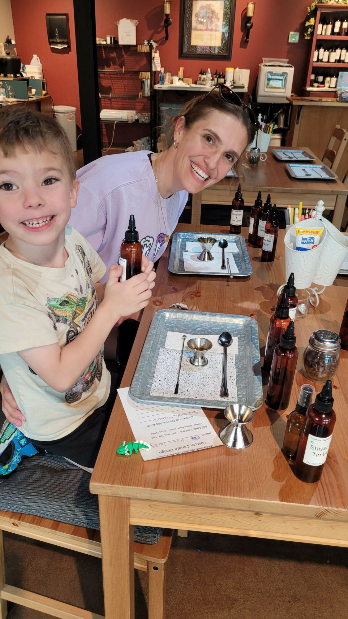 Two children sitting at a table with bottles, glasses, and a menu, smiling at the camera.