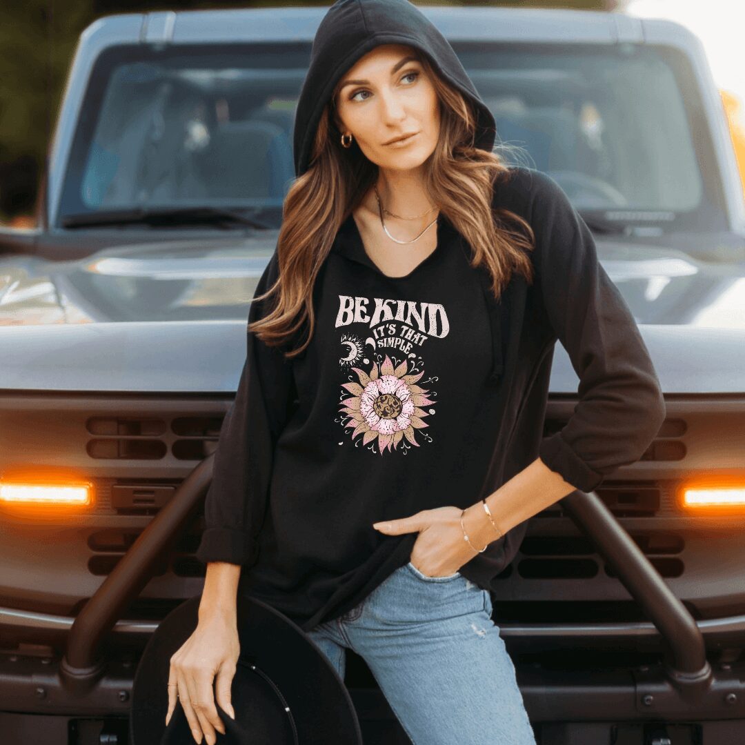 Young woman with long hair wearing a black hoodie and jeans, standing in front of a vehicle outdoors.
