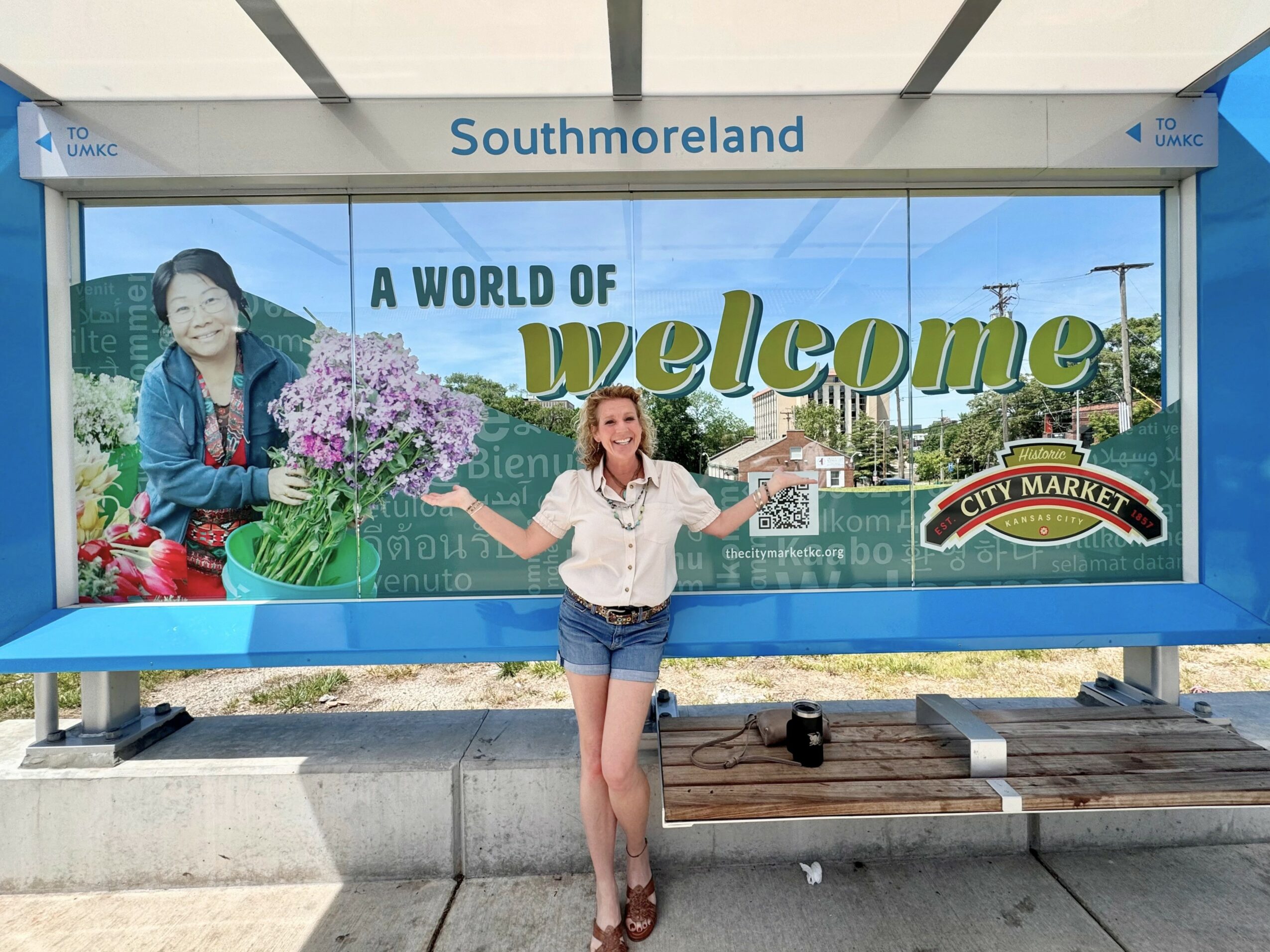 Person standing at Southmoreland bus stop with a large welcome sign and a woman holding a bouquet of flowers.