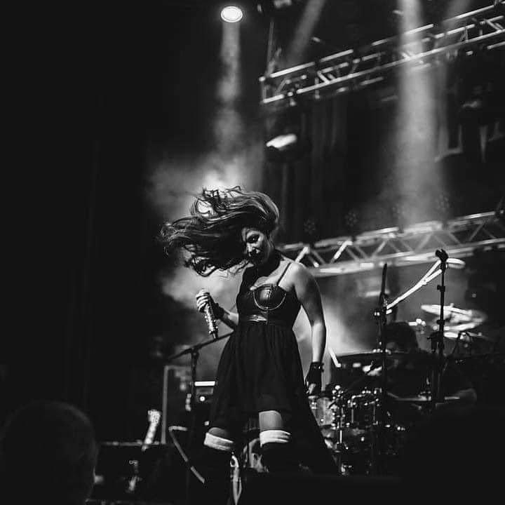 A woman with long hair dancing on stage with stage lights and musical instruments in the background.