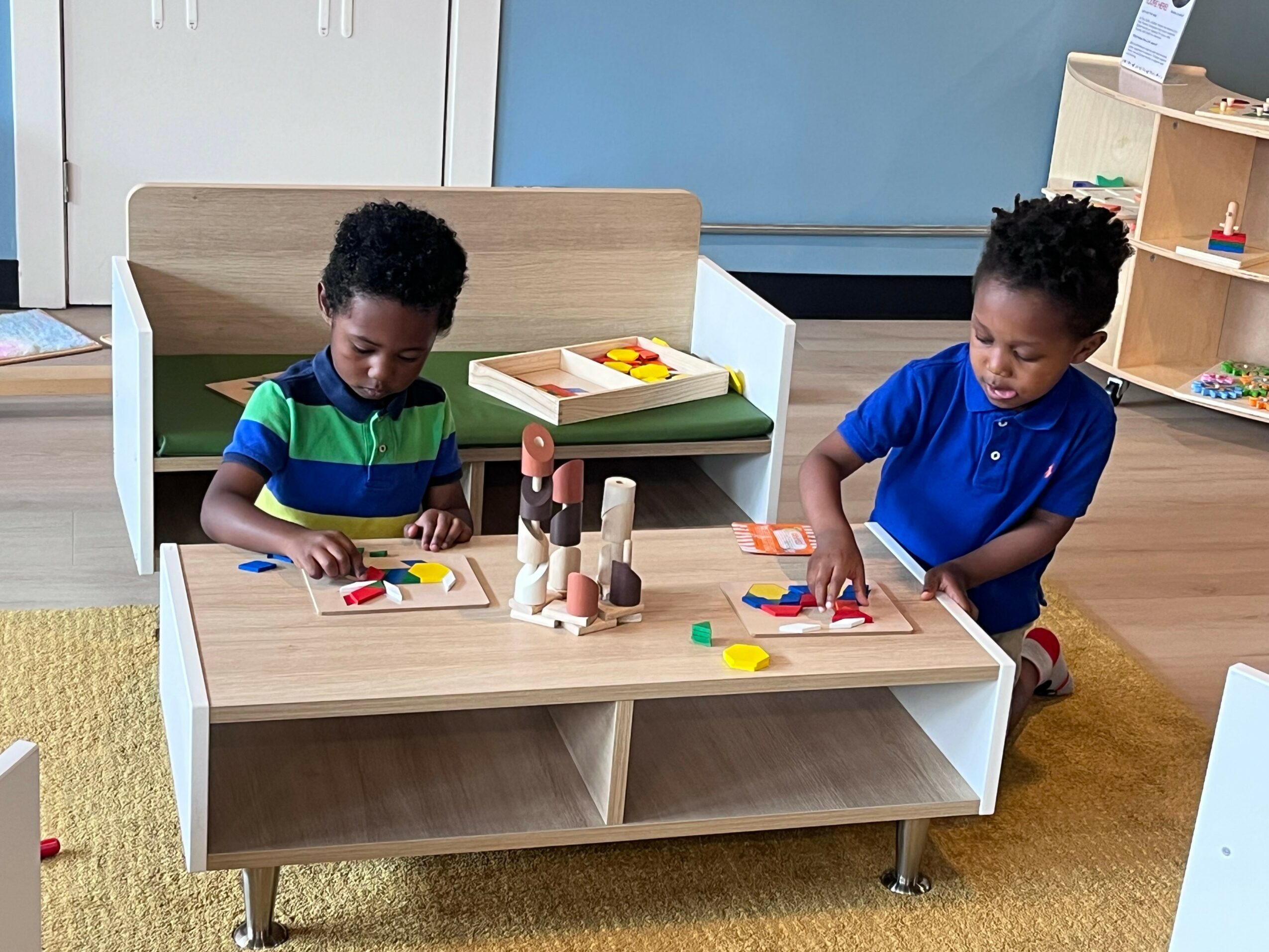 Two children playing with wooden blocks and colorful toys at a small table in a classroom.