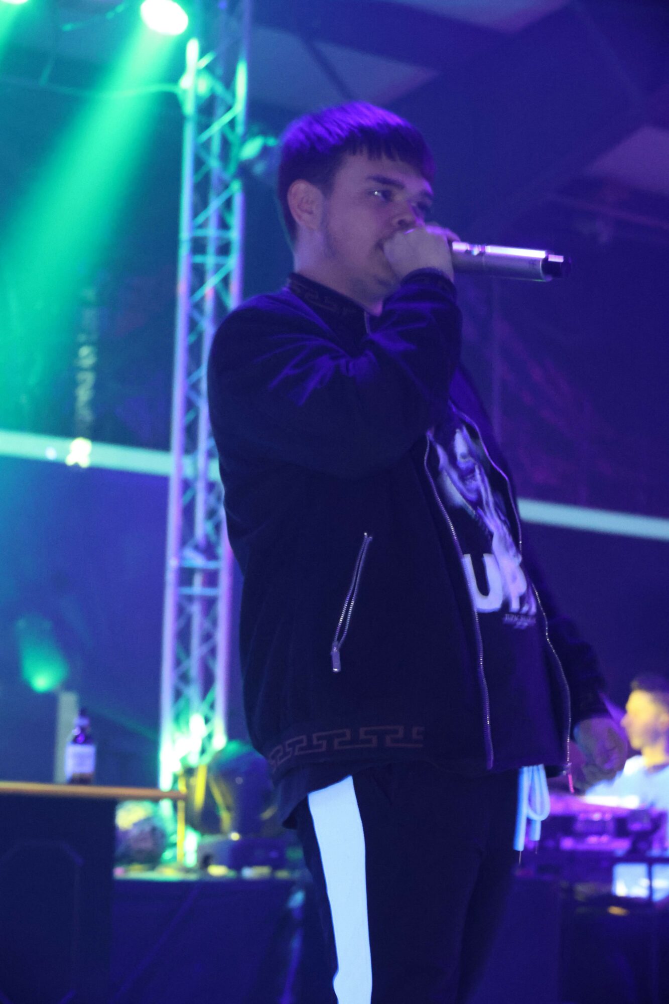 Person performing on stage with colorful lights and equipment in background.