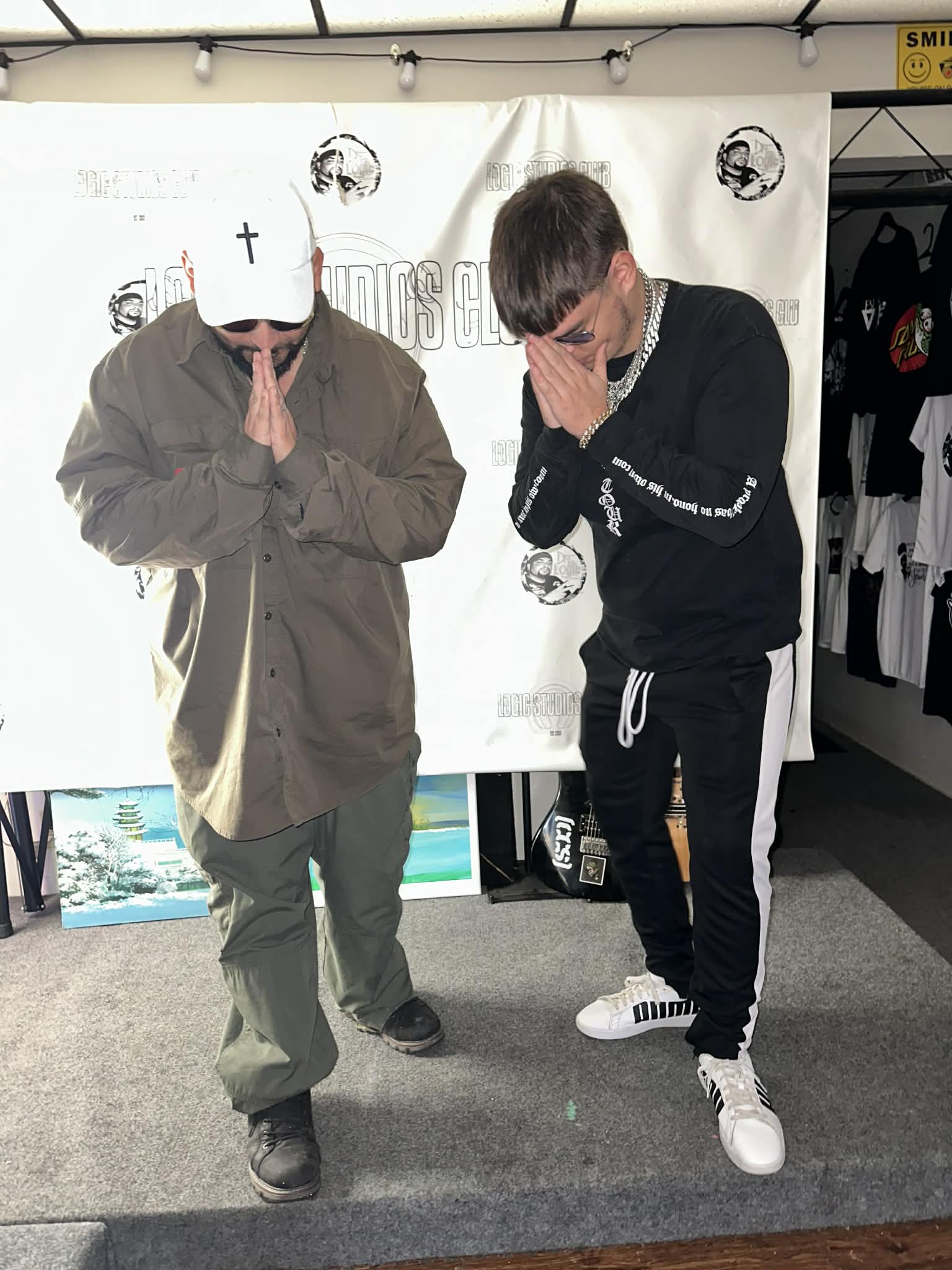 Two people with masks covering their faces, standing with hands pressed together in front of a white backdrop.