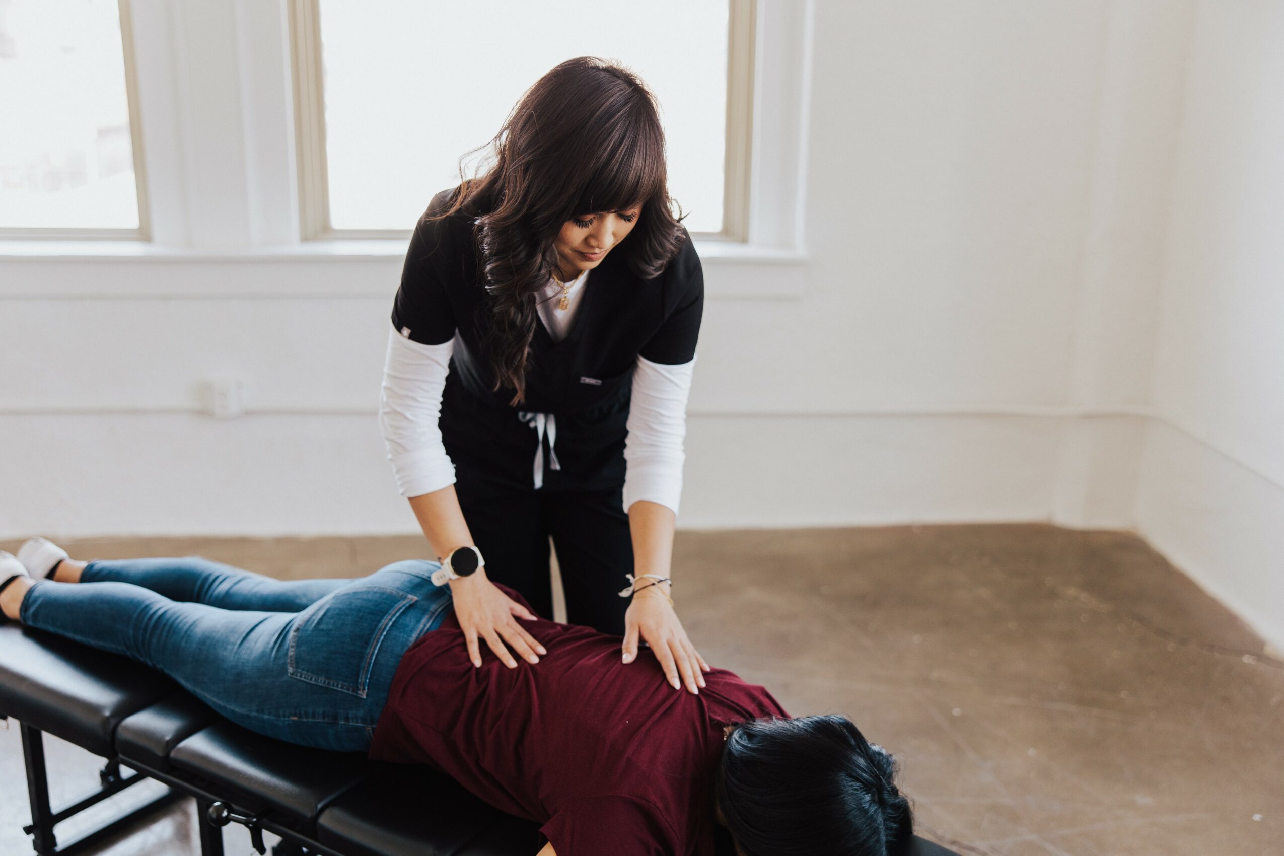 Person performing a massage on another person lying on a massage table in a bright room.