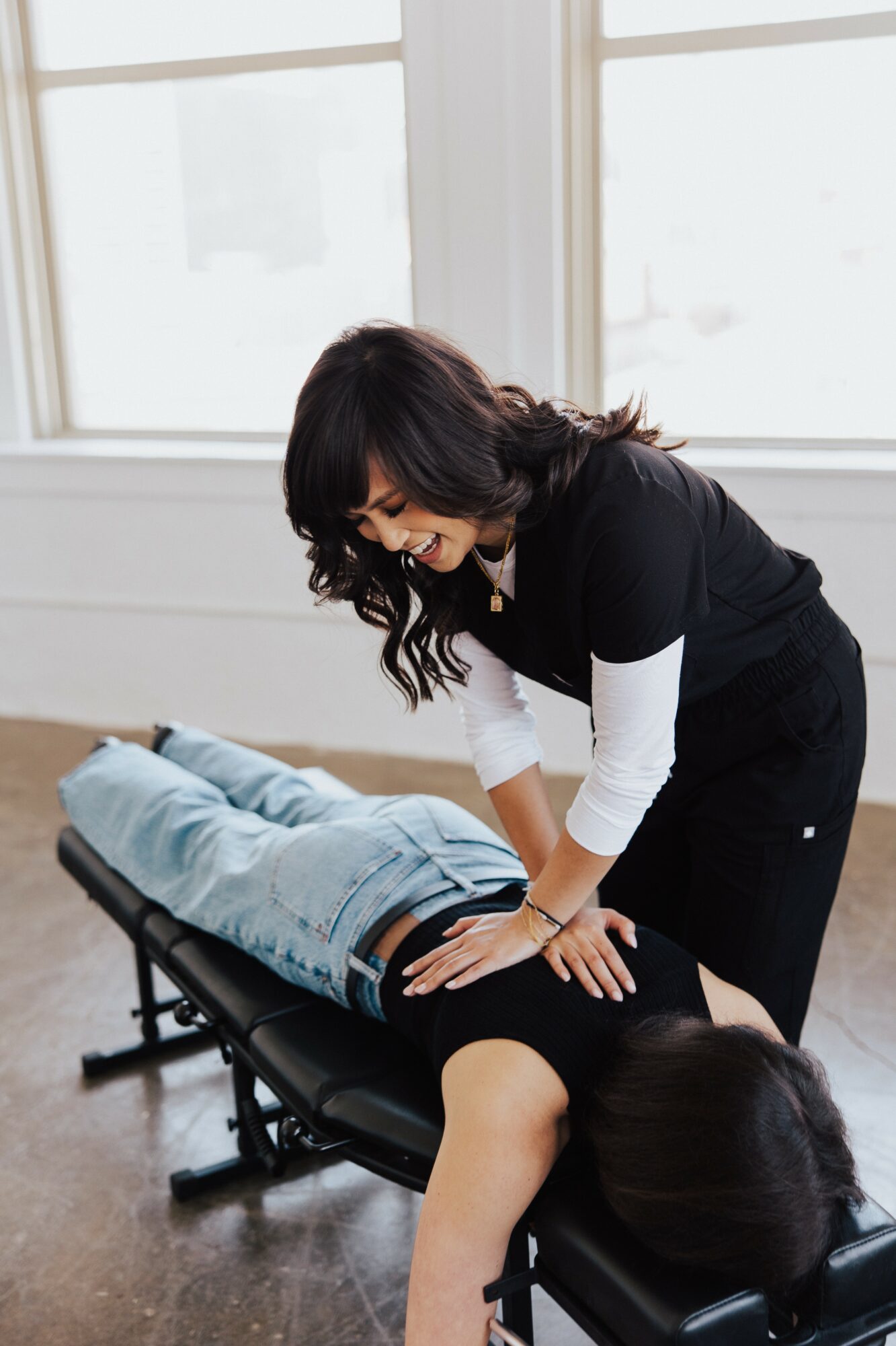Woman performing chiropractic adjustment on a person lying face down on a treatment table in a bright room.