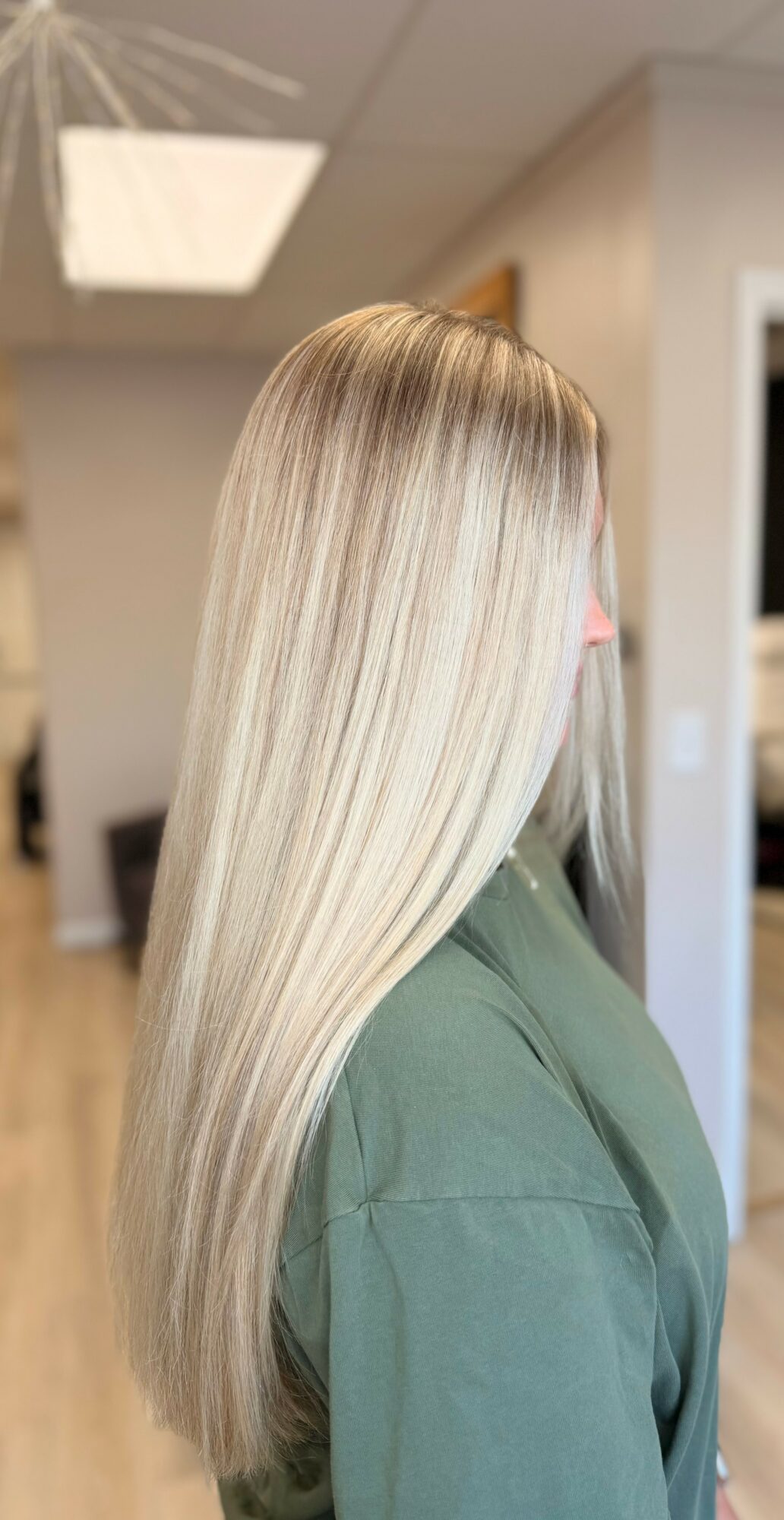 Side view of a woman with long, straight, blonde hair in an indoor setting.