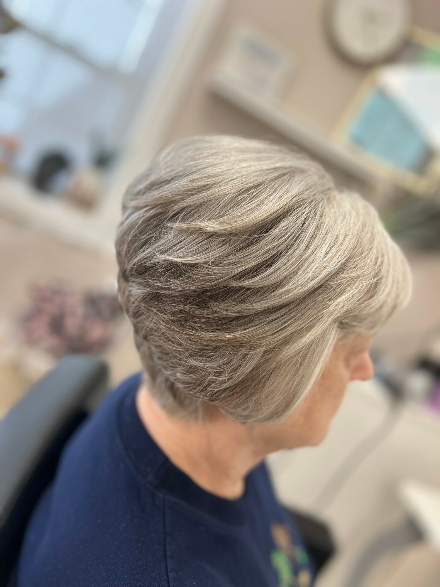 Side view of a woman with short, layered gray hair in an indoor setting.