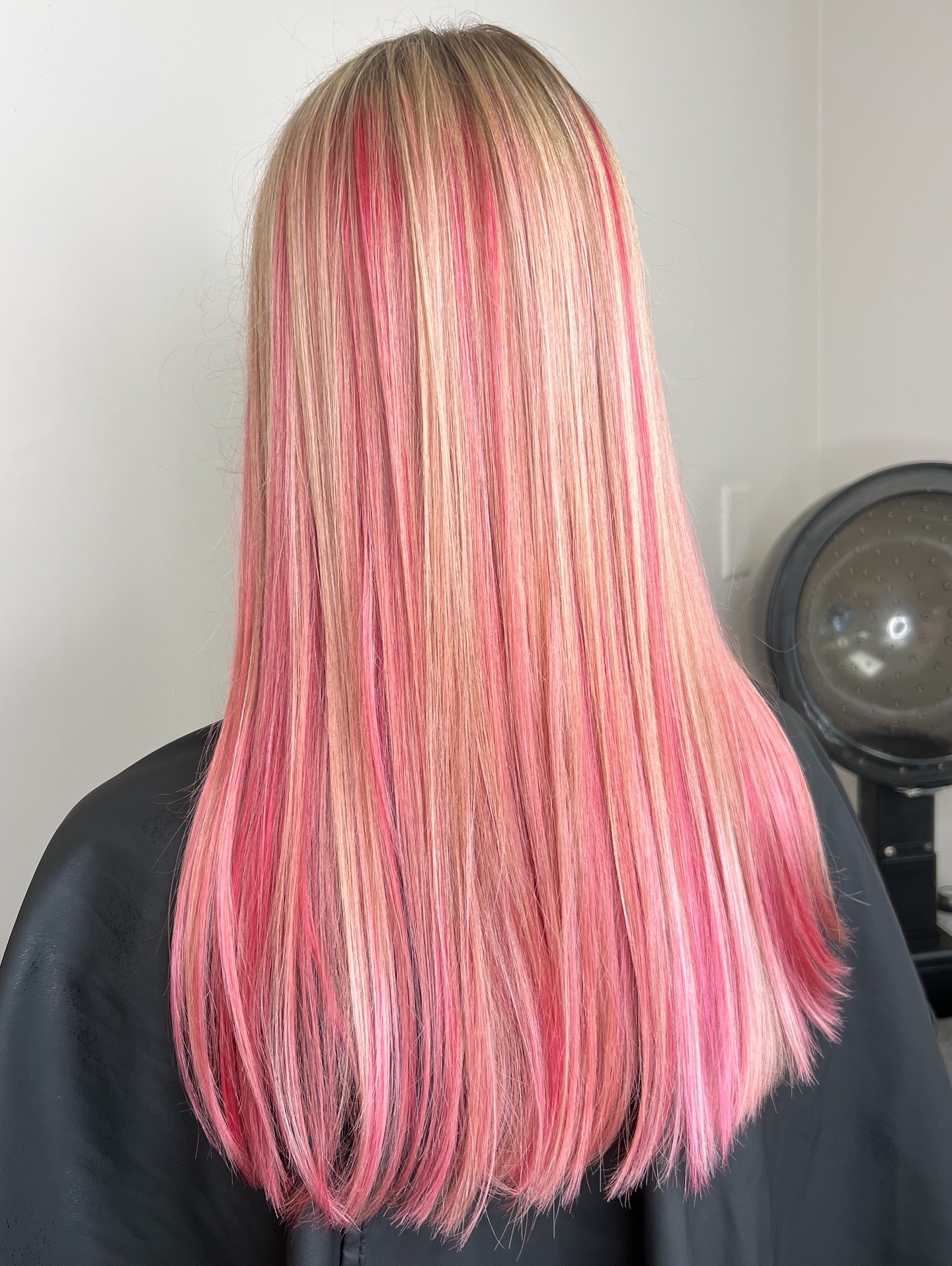 Back view of long, straight hair with pink and blonde highlights, in a salon setting.