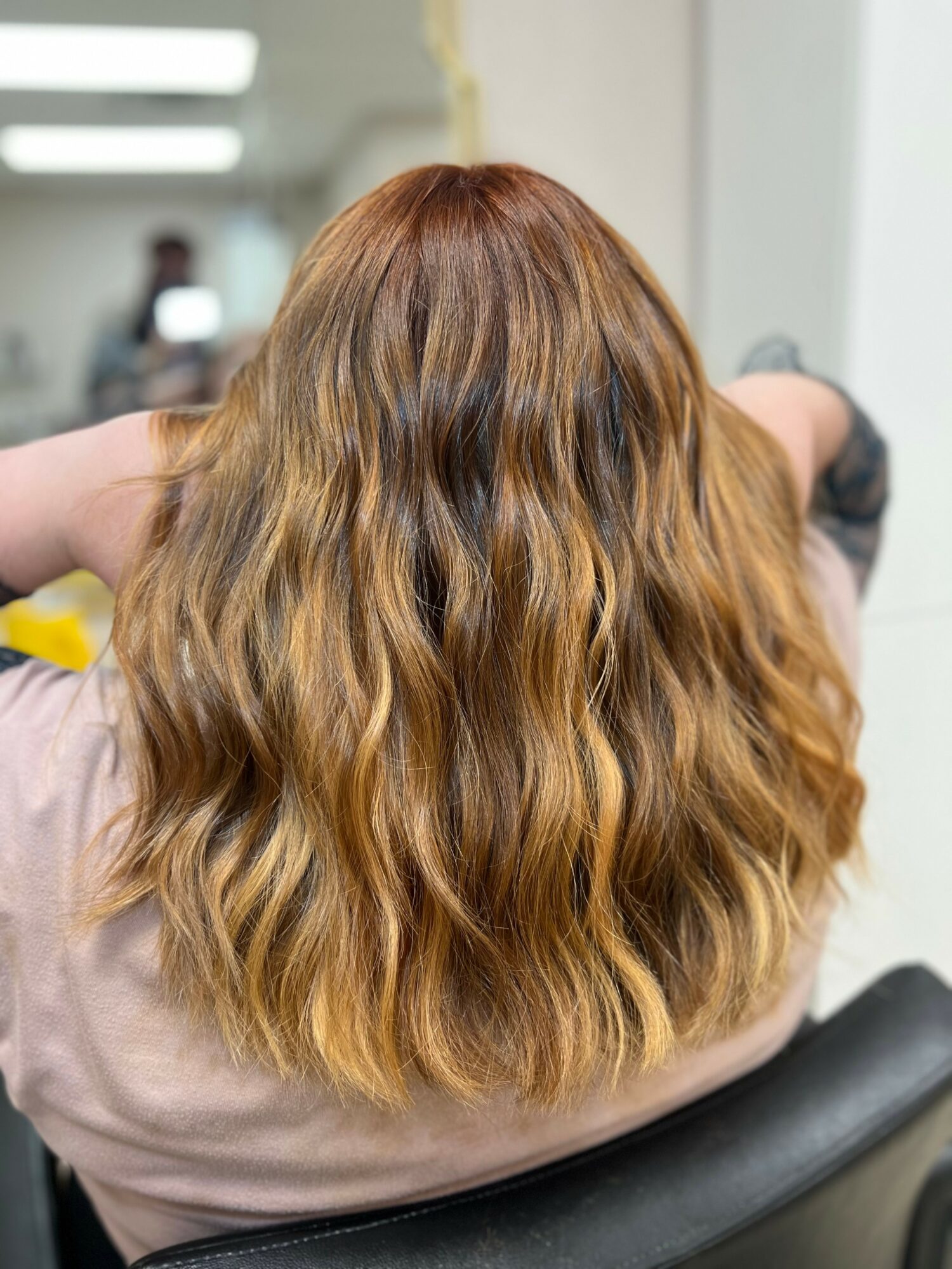 Back of a person with long, wavy, light brown hair sitting in a chair indoors.