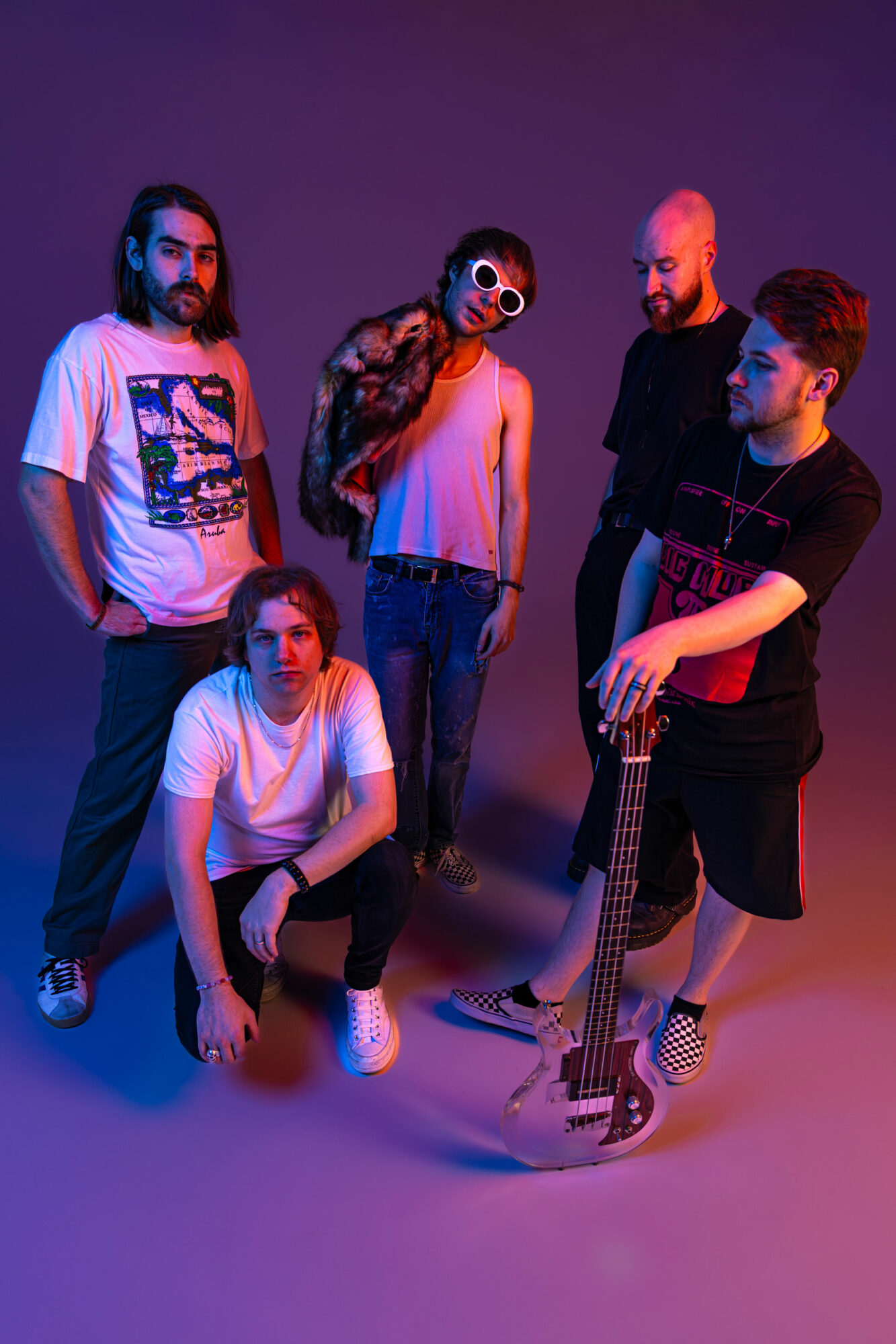 Group of five people with colorful lighting, one holding a guitar, posing against a purple background.