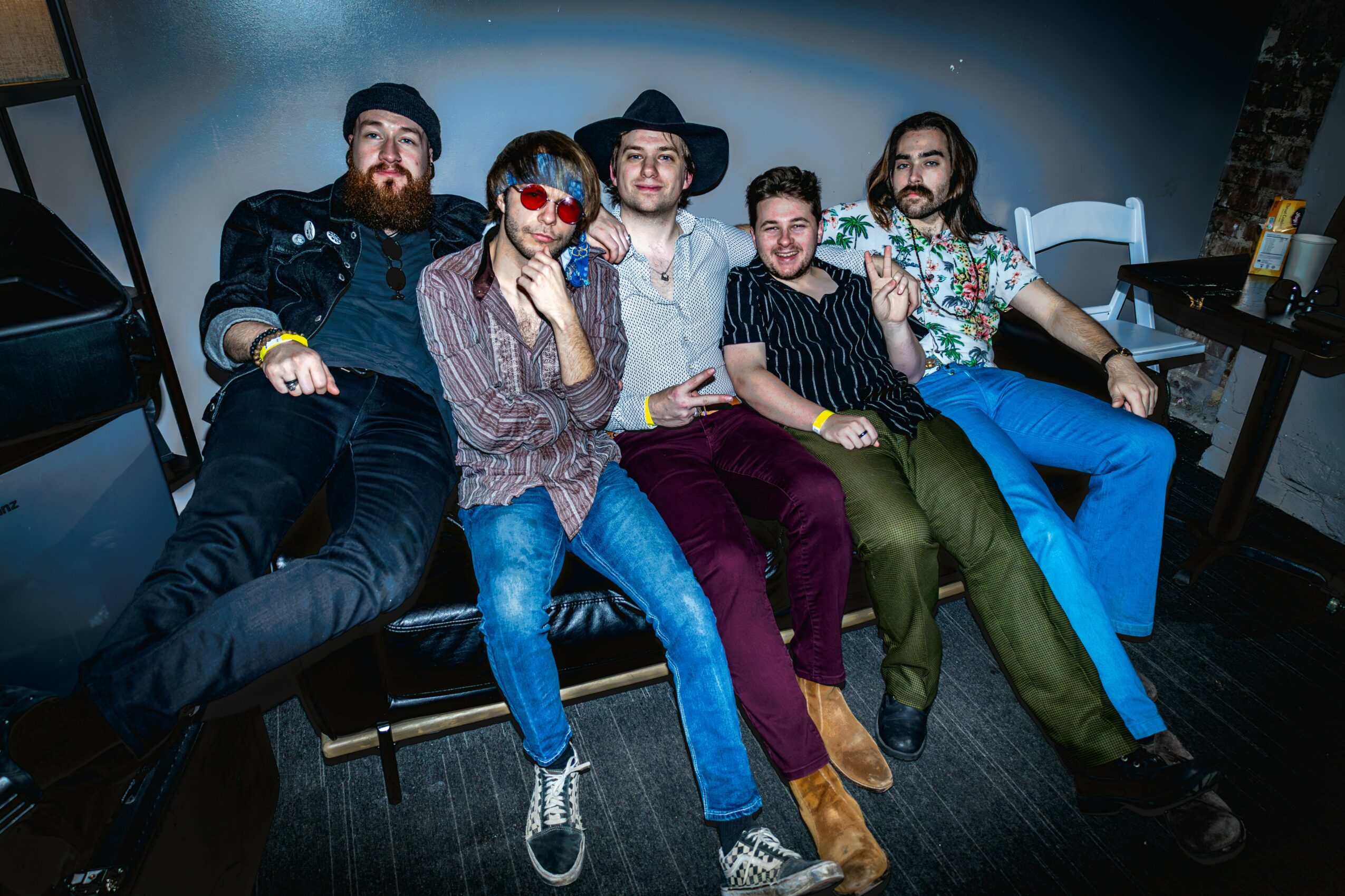 Five people sitting on a couch, smiling, in a room with a dark floor and a table with drinks.