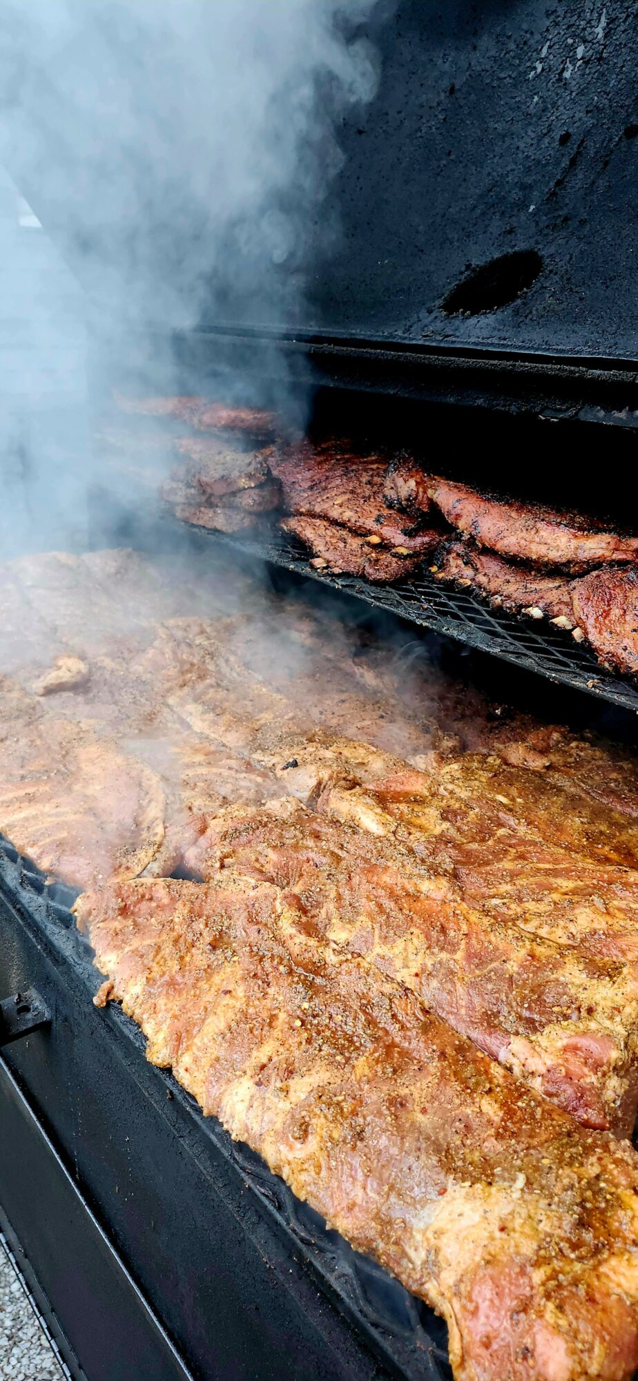 Barbecue grill with meat cooking, smoke rising, and a dark background.
