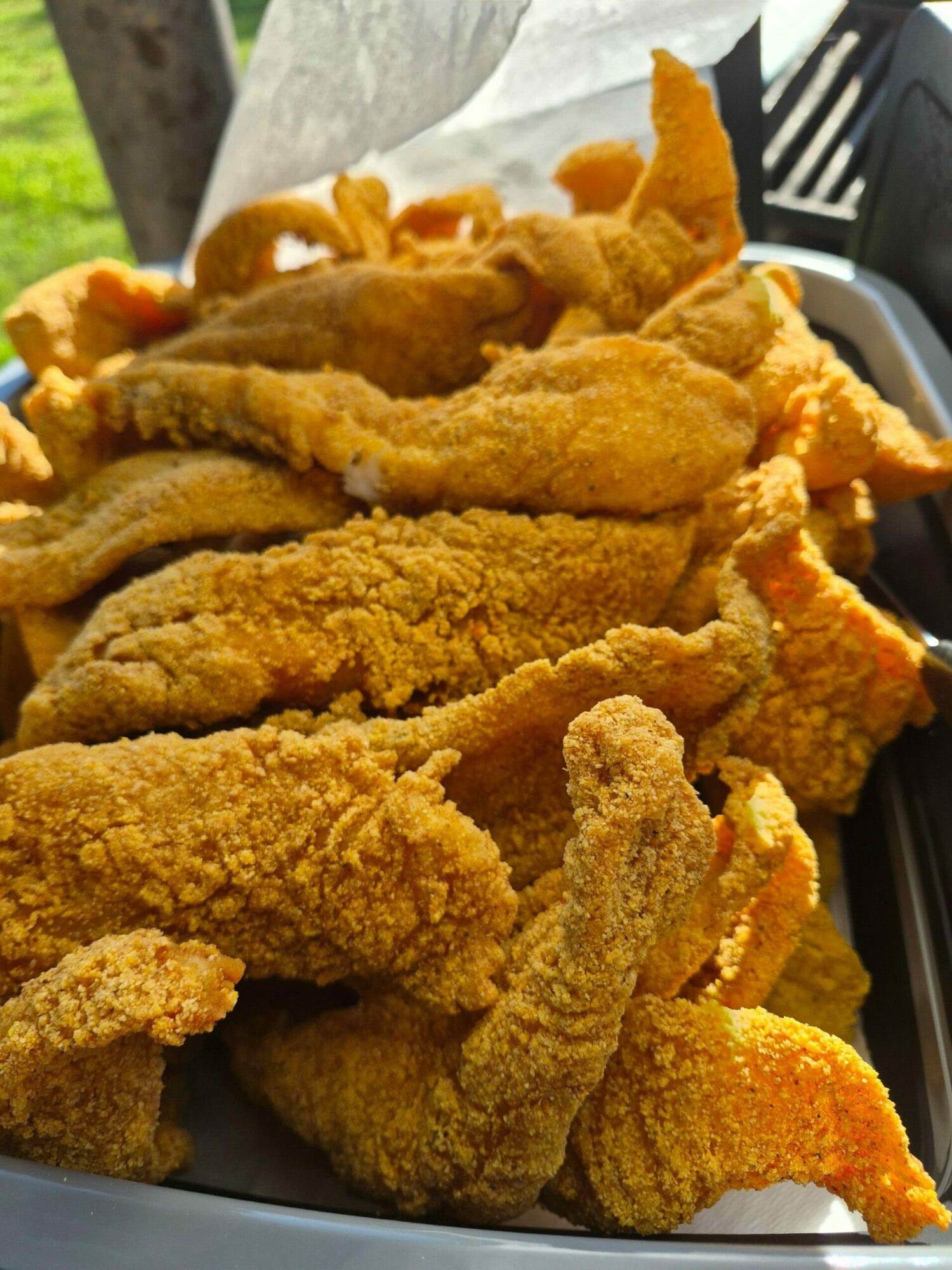 Close-up of fried chicken pieces on a tray, golden-brown and crispy, with some paper lining on the side.