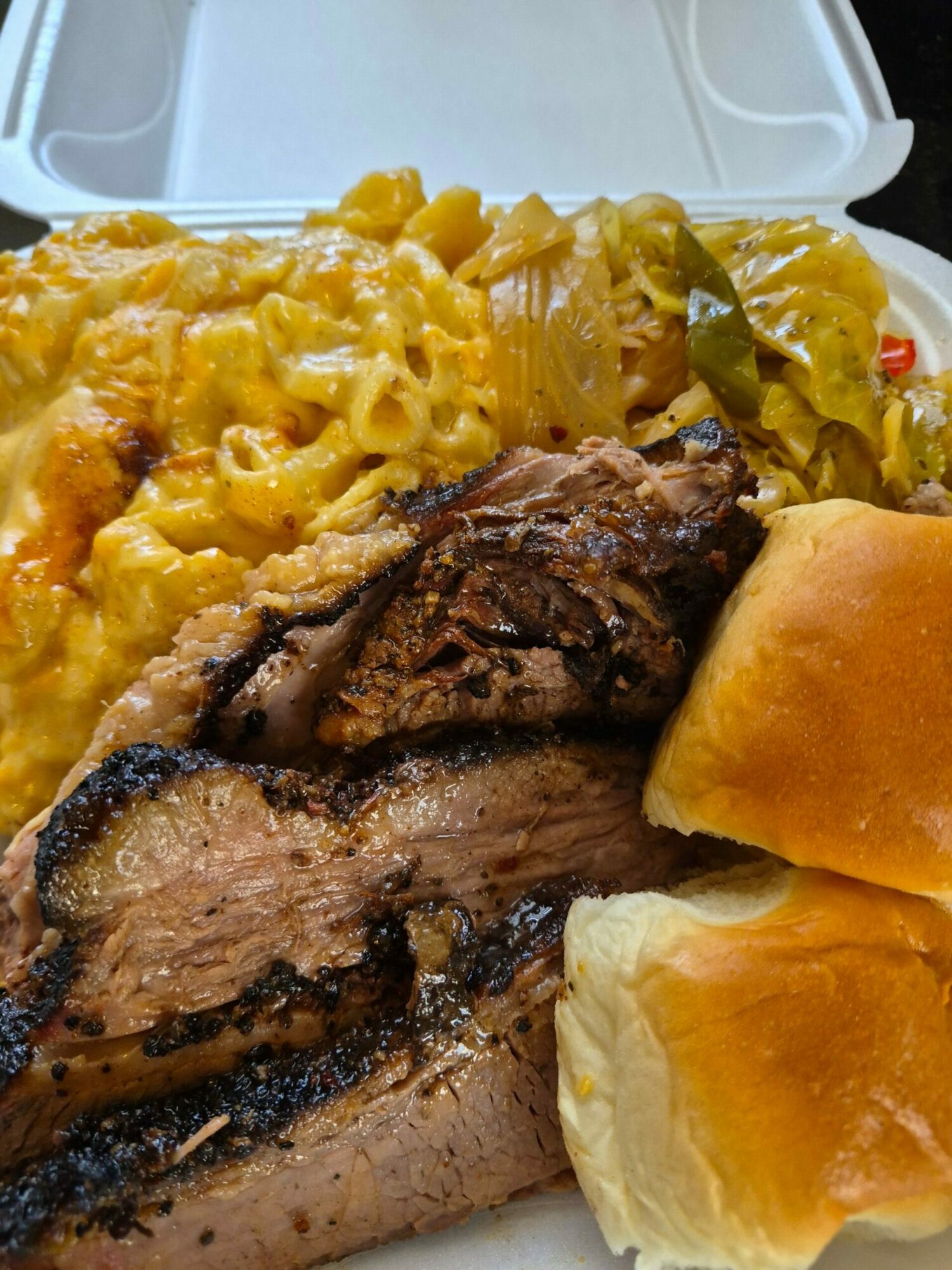 Barbecue ribs with bread rolls and pickles on a plate, close-up view.