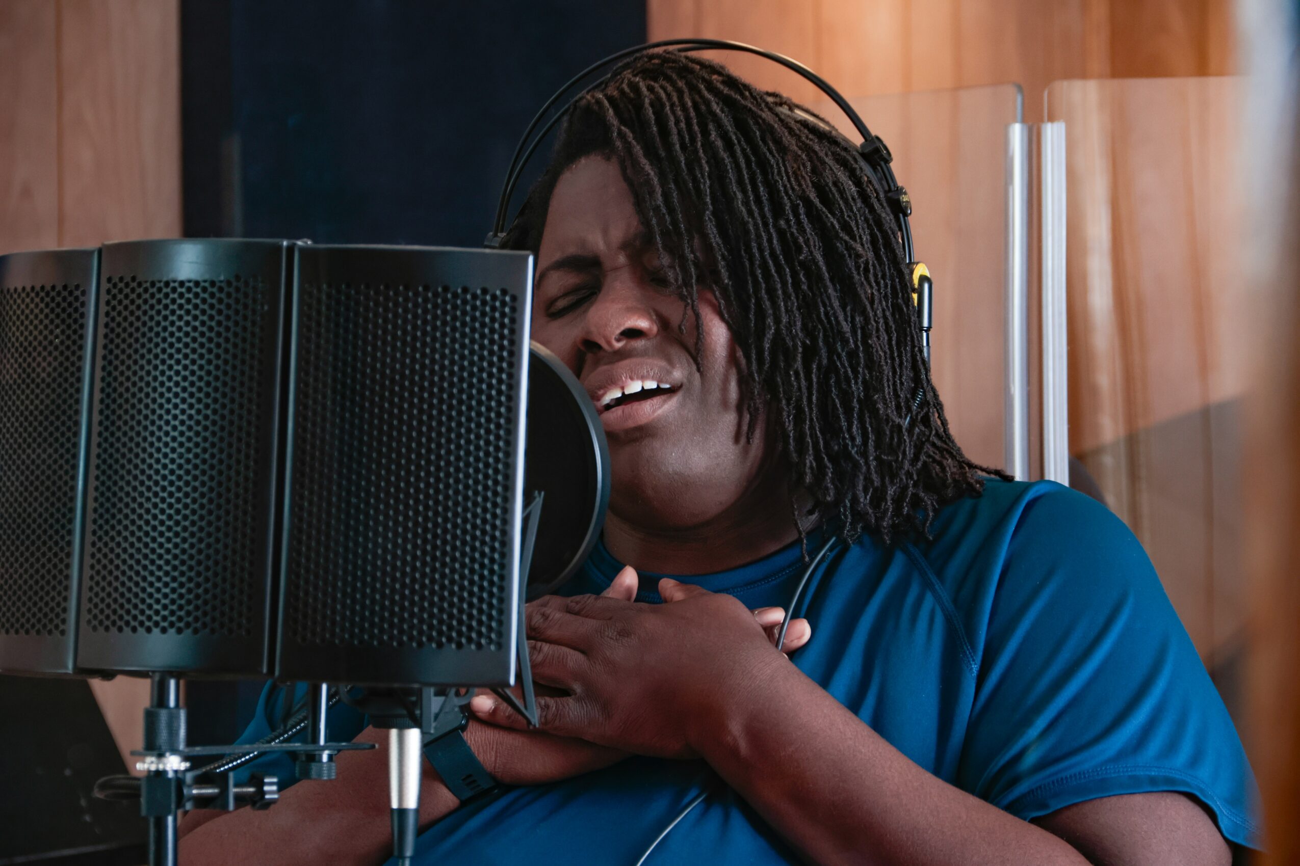 Woman singing passionately into a microphone in a recording studio, with her eyes closed and hands on her chest.