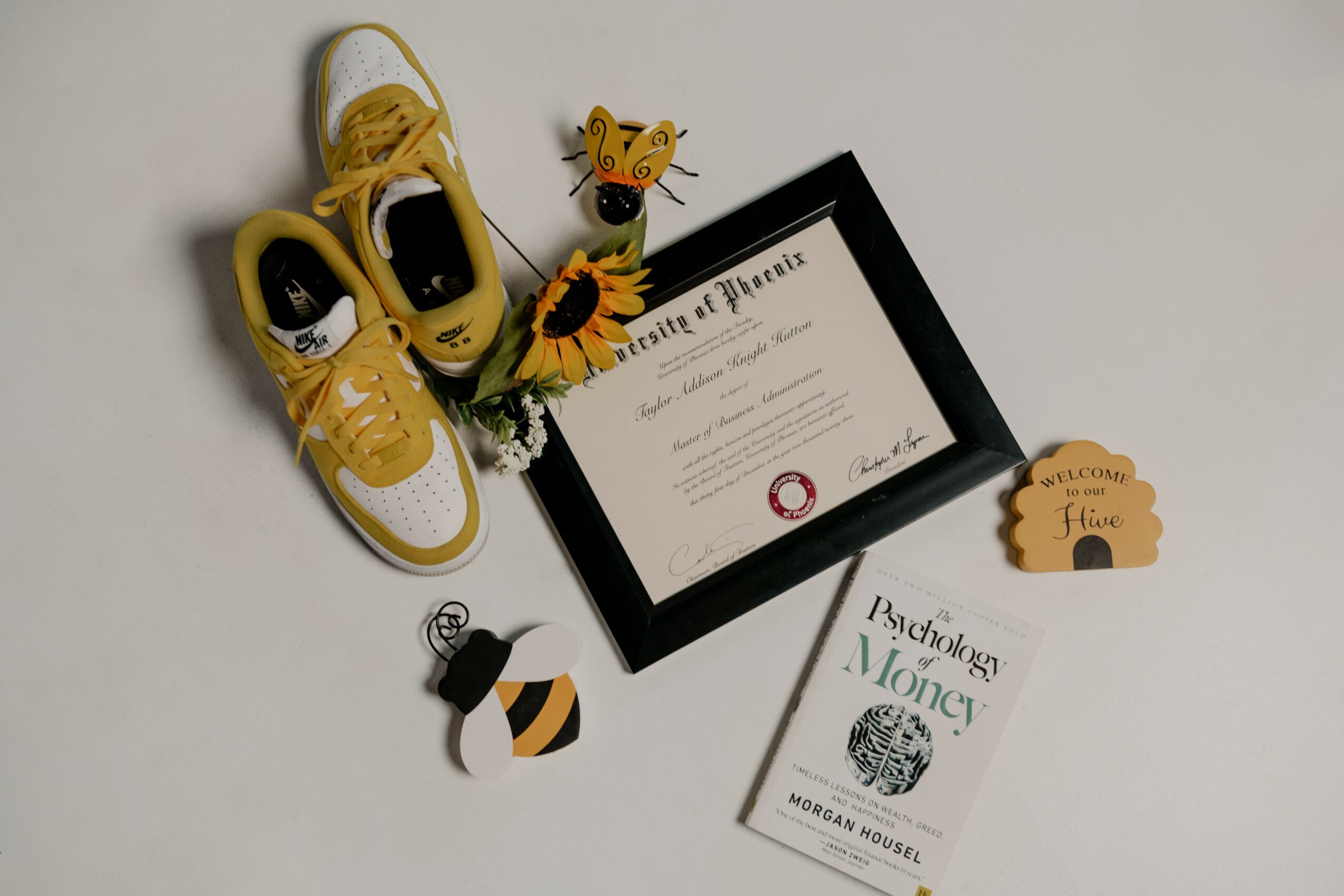 Yellow sneakers, a framed certificate, a bee and flower decoration, and a small welcome sign on a white surface.