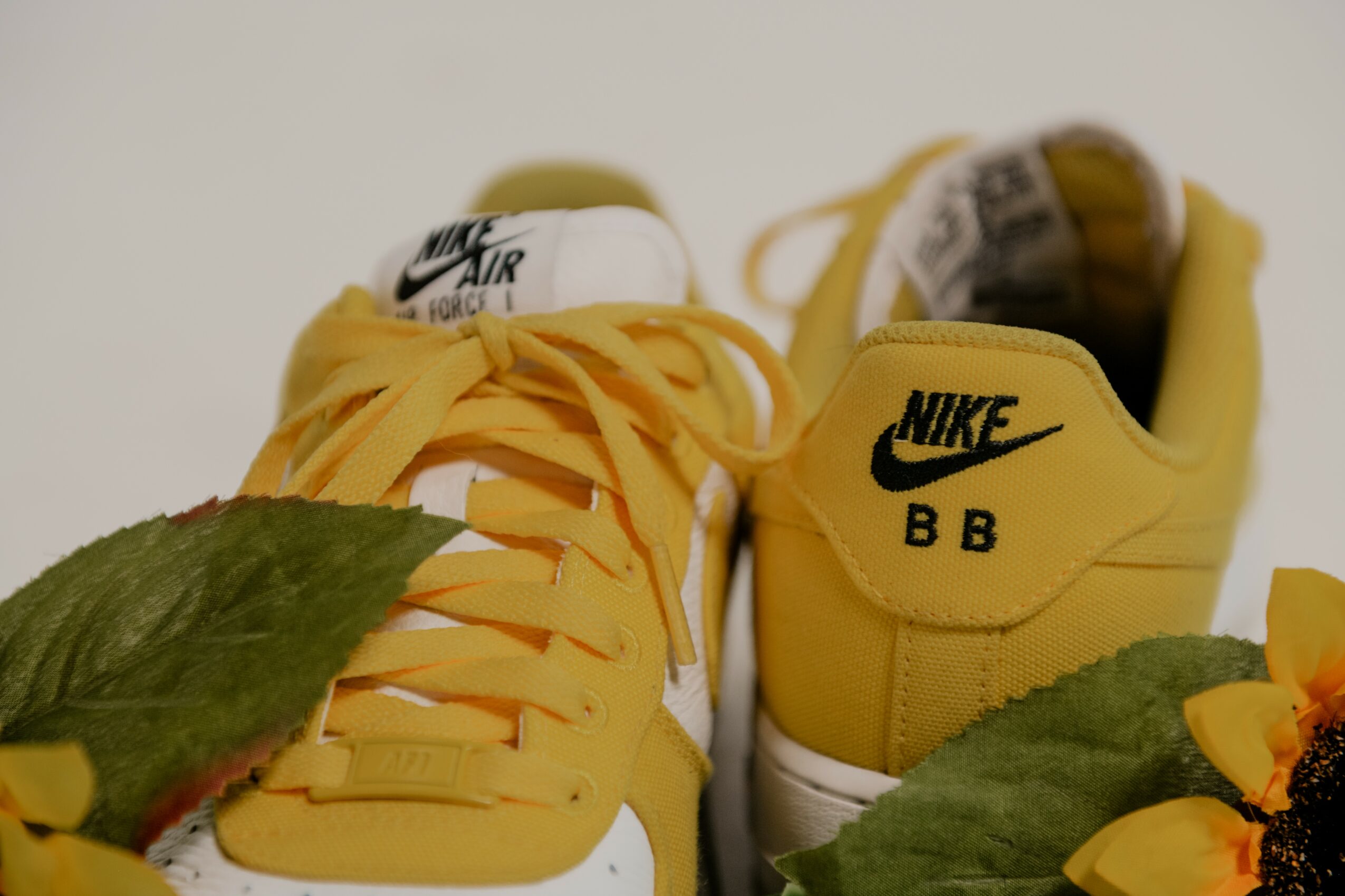 Pair of yellow Nike sneakers with green leaves and yellow flowers in front, plain background