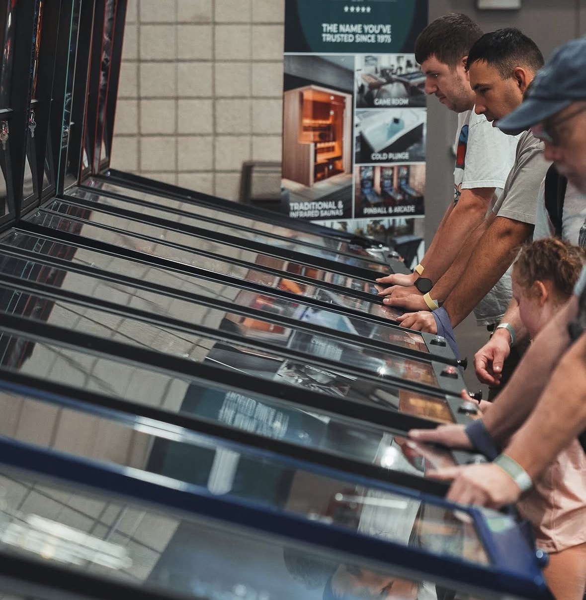 People browsing items in a store, looking at display cases with glass tops, in a well-lit indoor space.