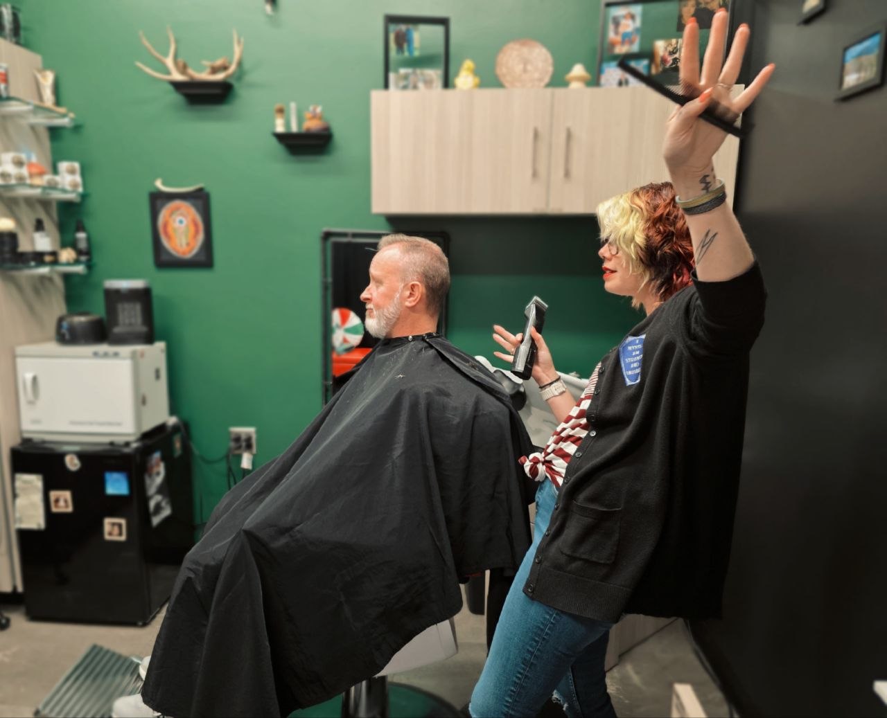 Person getting a haircut in a salon, with a stylist holding scissors and a comb, and another person raising a hand.