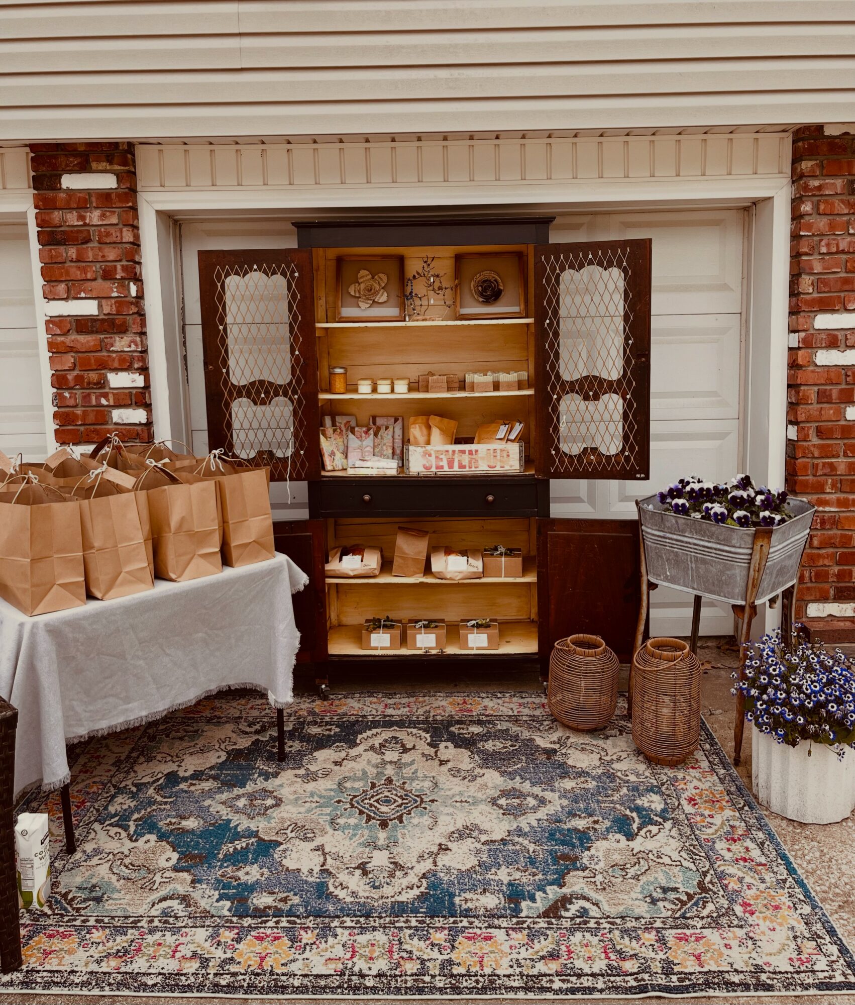 Display cabinet with open doors, shelves with decorative items, against a brick wall, with a patterned rug on the floor.