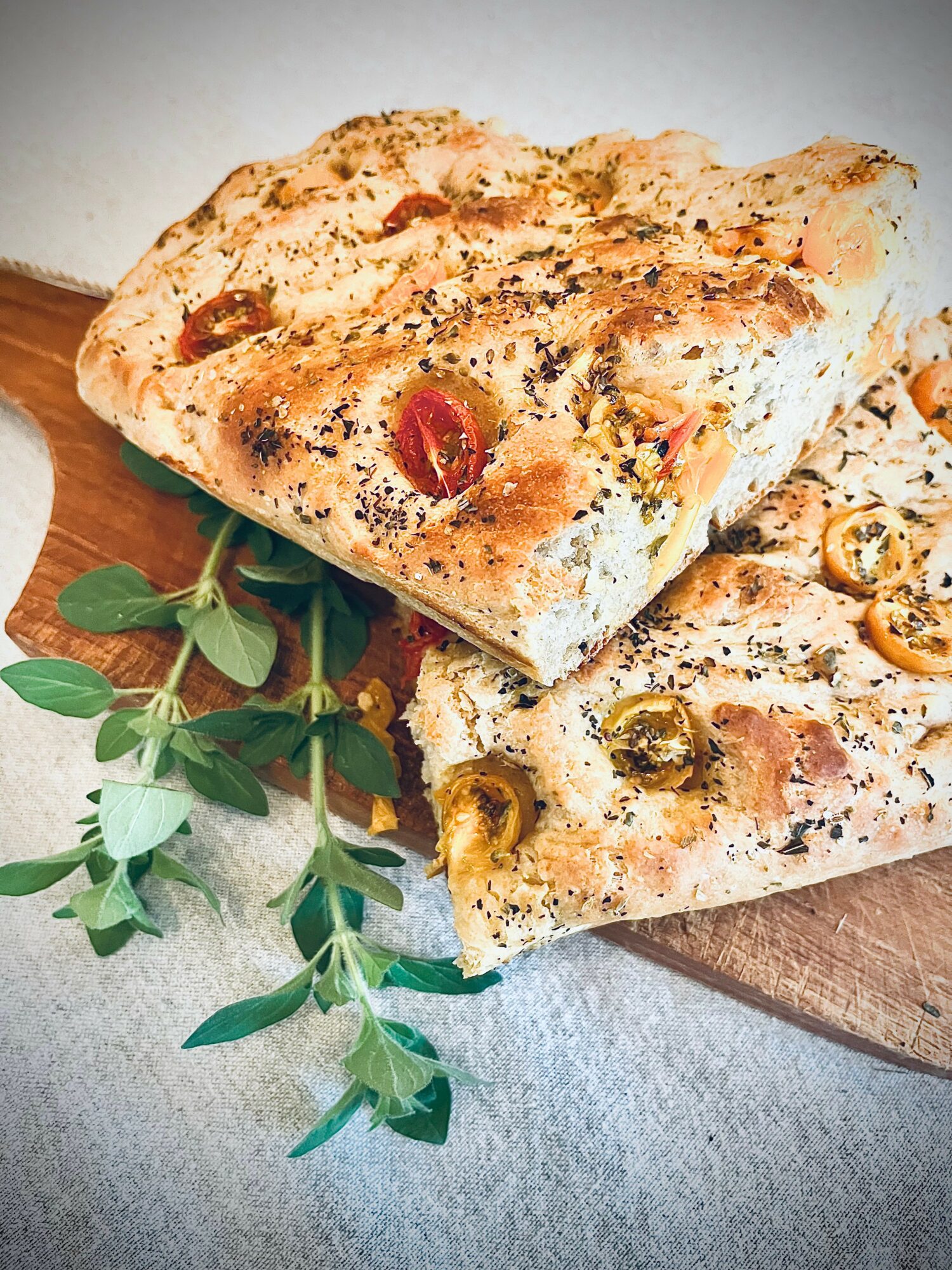 Two slices of pizza on a wooden board with herbs, cheese, and toppings, garnished with green leaves.