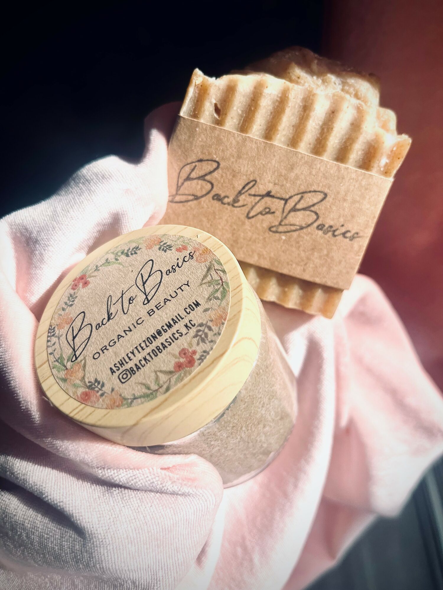 Hand holding a round soap and a wrapped soap with a ridged surface, both labeled 'Belt To Bric' in a pink cloth background.