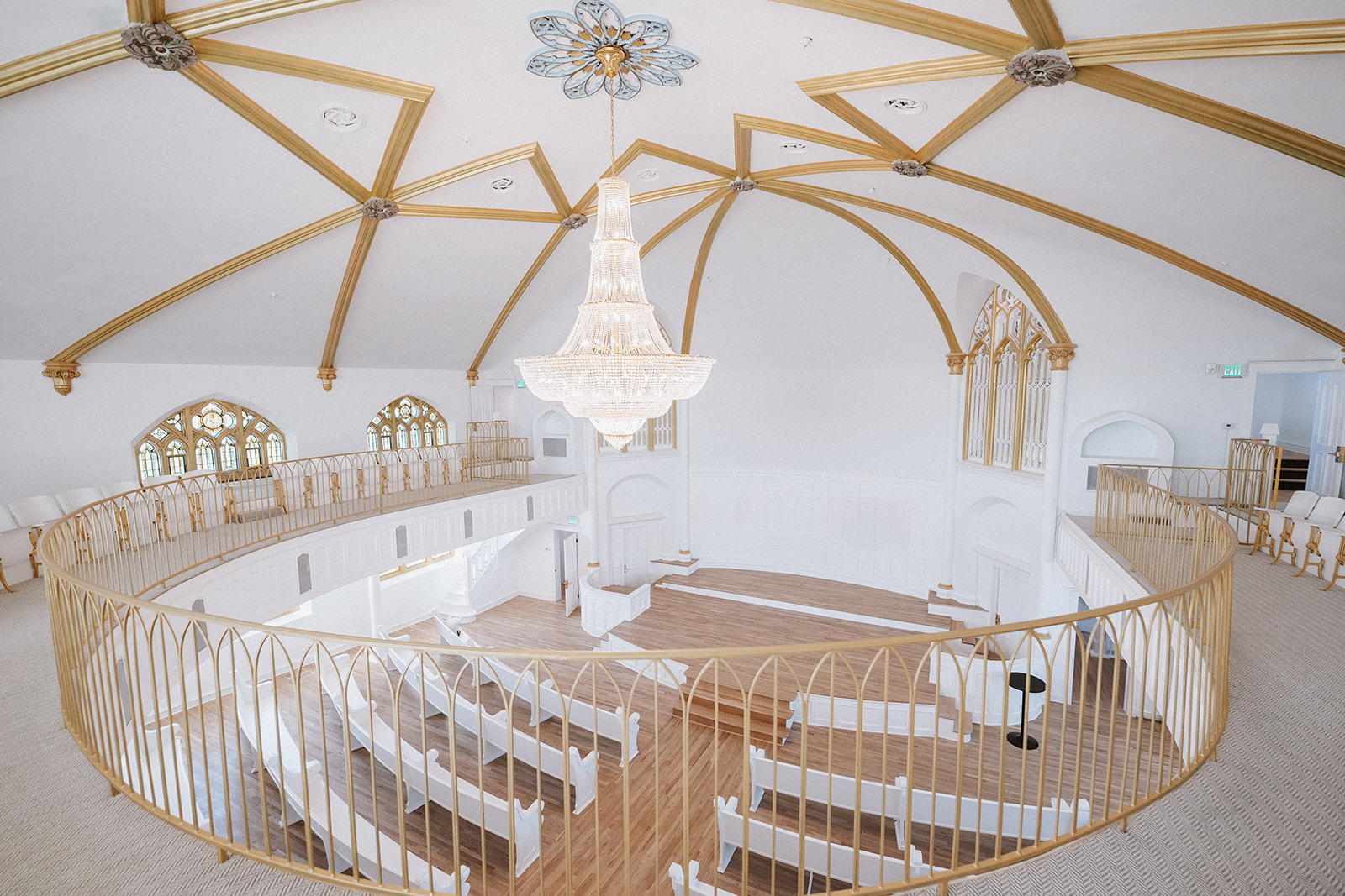Elegant circular room with a chandelier, gold accents, and white furniture, set up for a formal event or wedding.