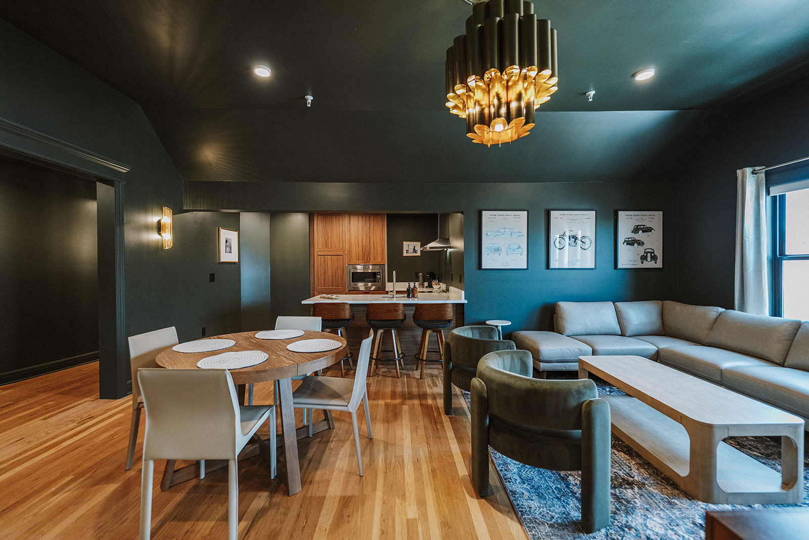Living room with dining area, modern furniture, wooden floor, dark walls, chandelier, and artwork on wall.
