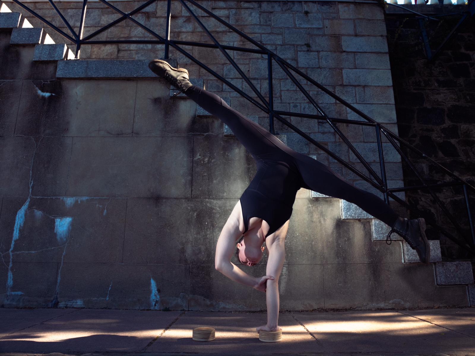 Person performing a handstand with legs resting on a railing, outdoors on a concrete surface.