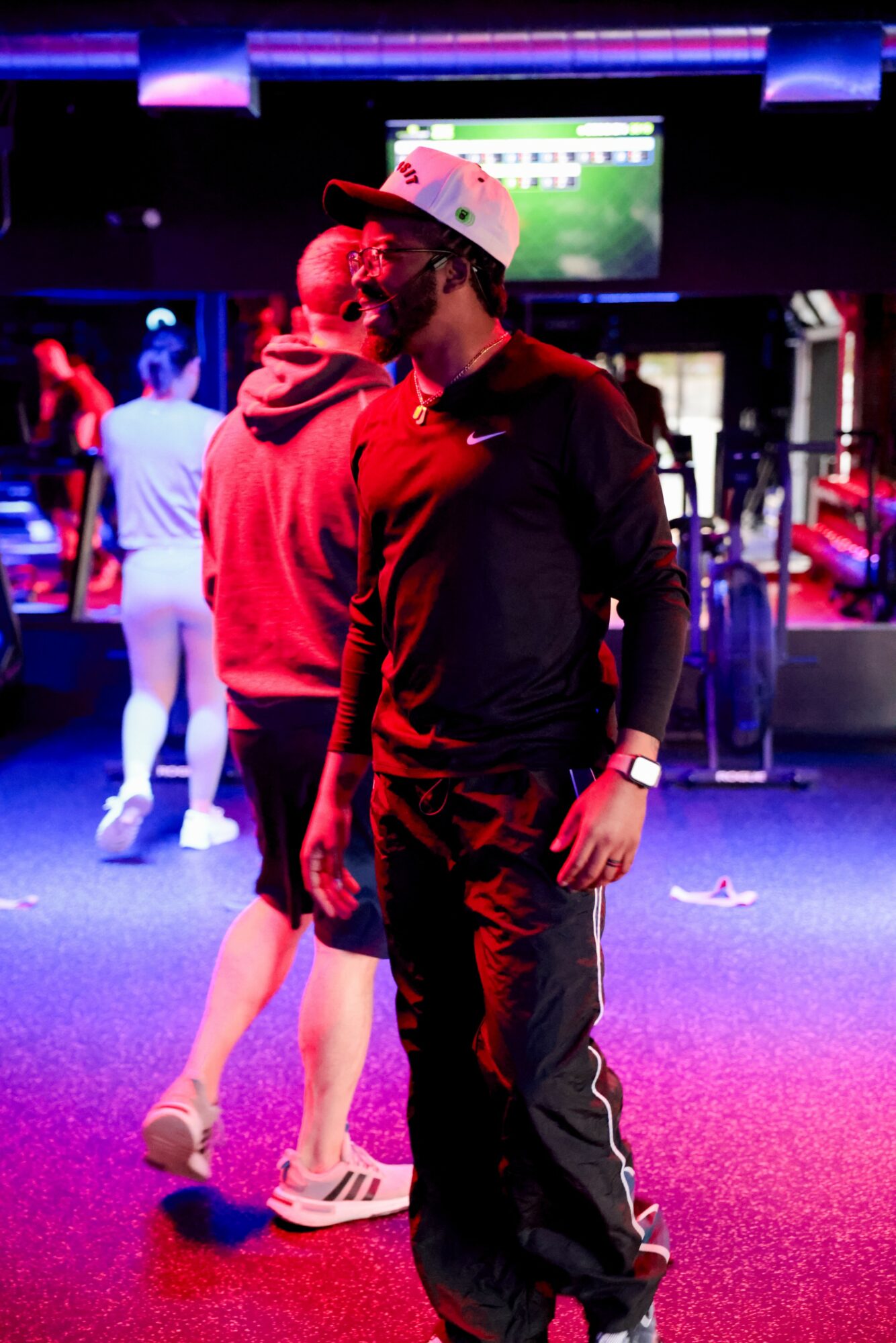 Two young men in a gaming arcade, one wearing a white cap and black jacket, the other in a red hoodie, with arcade machines in background.