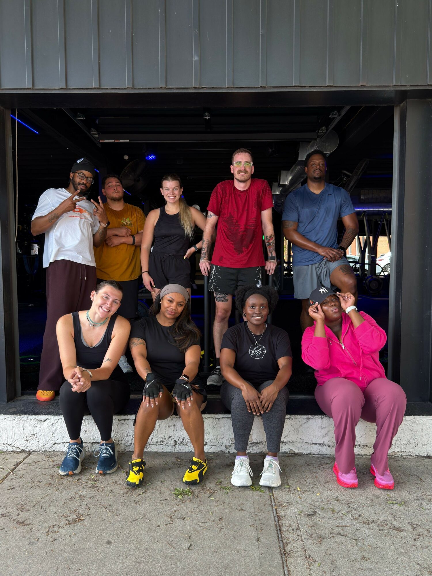 Group of seven people posing outdoors, some making peace signs, in front of a building entrance.