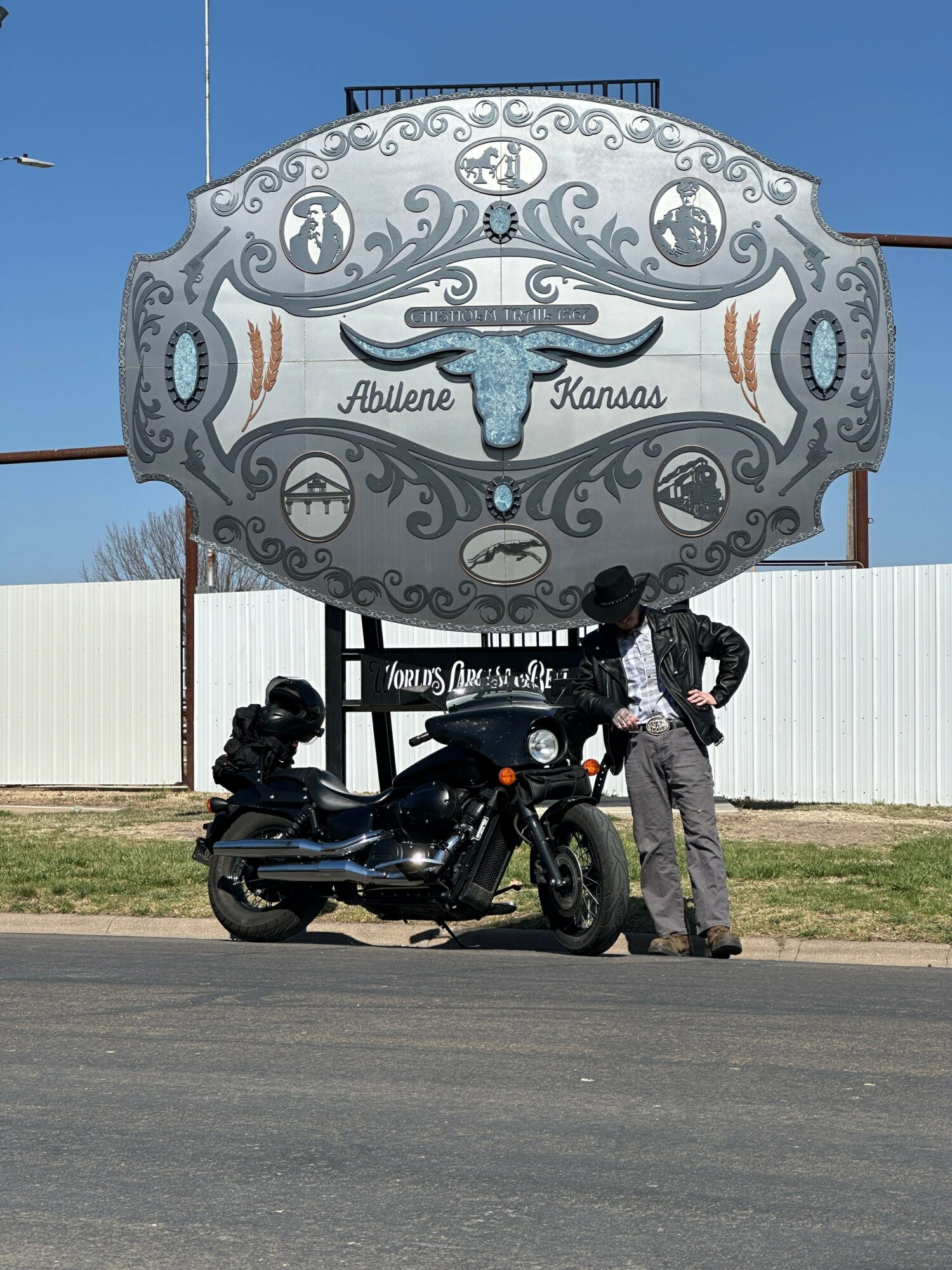 Person standing next to a motorcycle in front of a decorative sign with a whale illustration, on a sunny day.