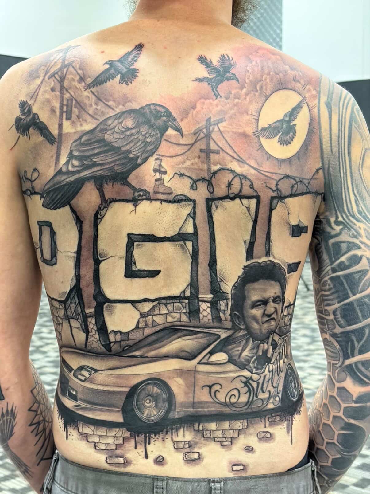 Tattoo of a large bird, cityscape, and a man with a car on the person's back, with various smaller birds and elements.