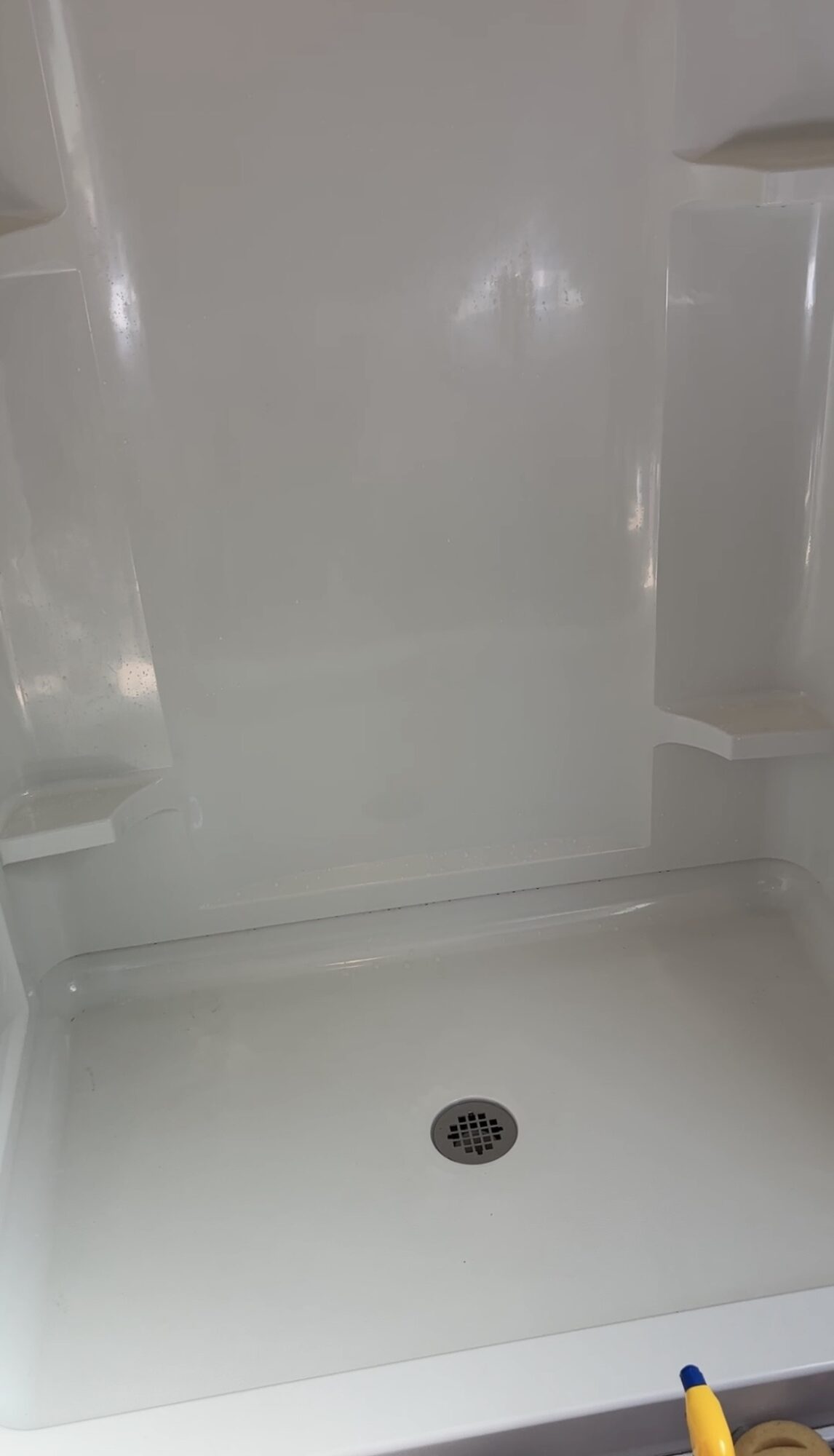 Empty refrigerator interior with shelves and a drain at the bottom.