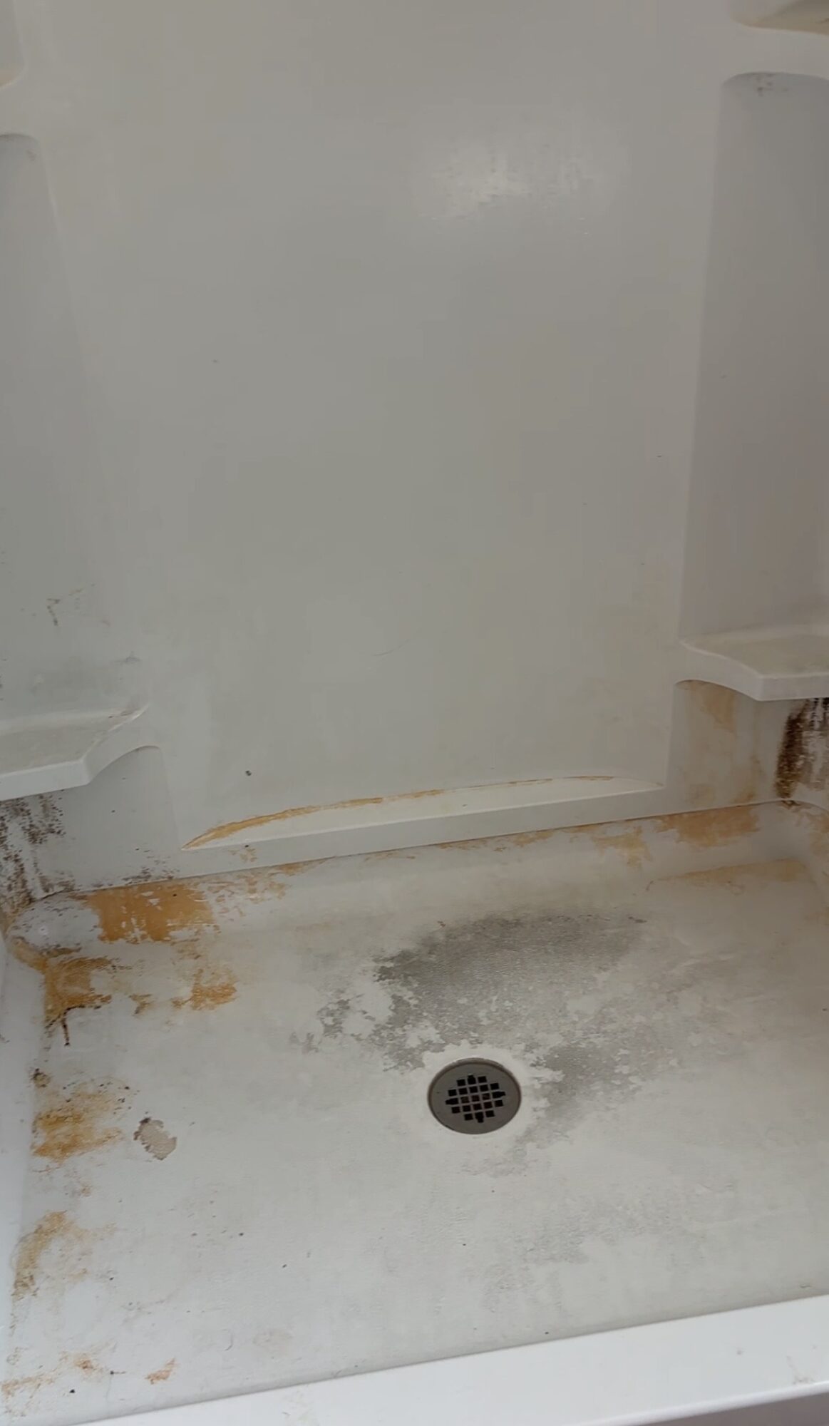 Shower floor with drain, rust stains, and water damage on the wall and floor.