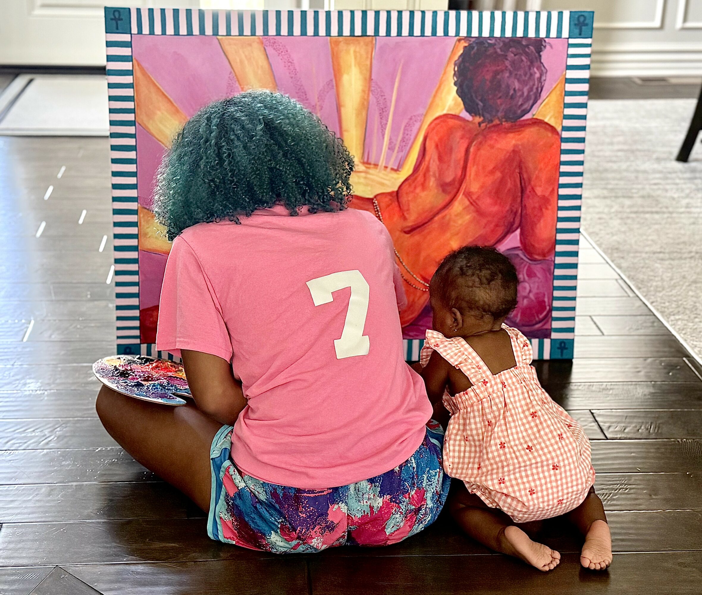 Adult and child sitting on floor, painting a colorful artwork on a large canvas, with bright sun rays in the background.