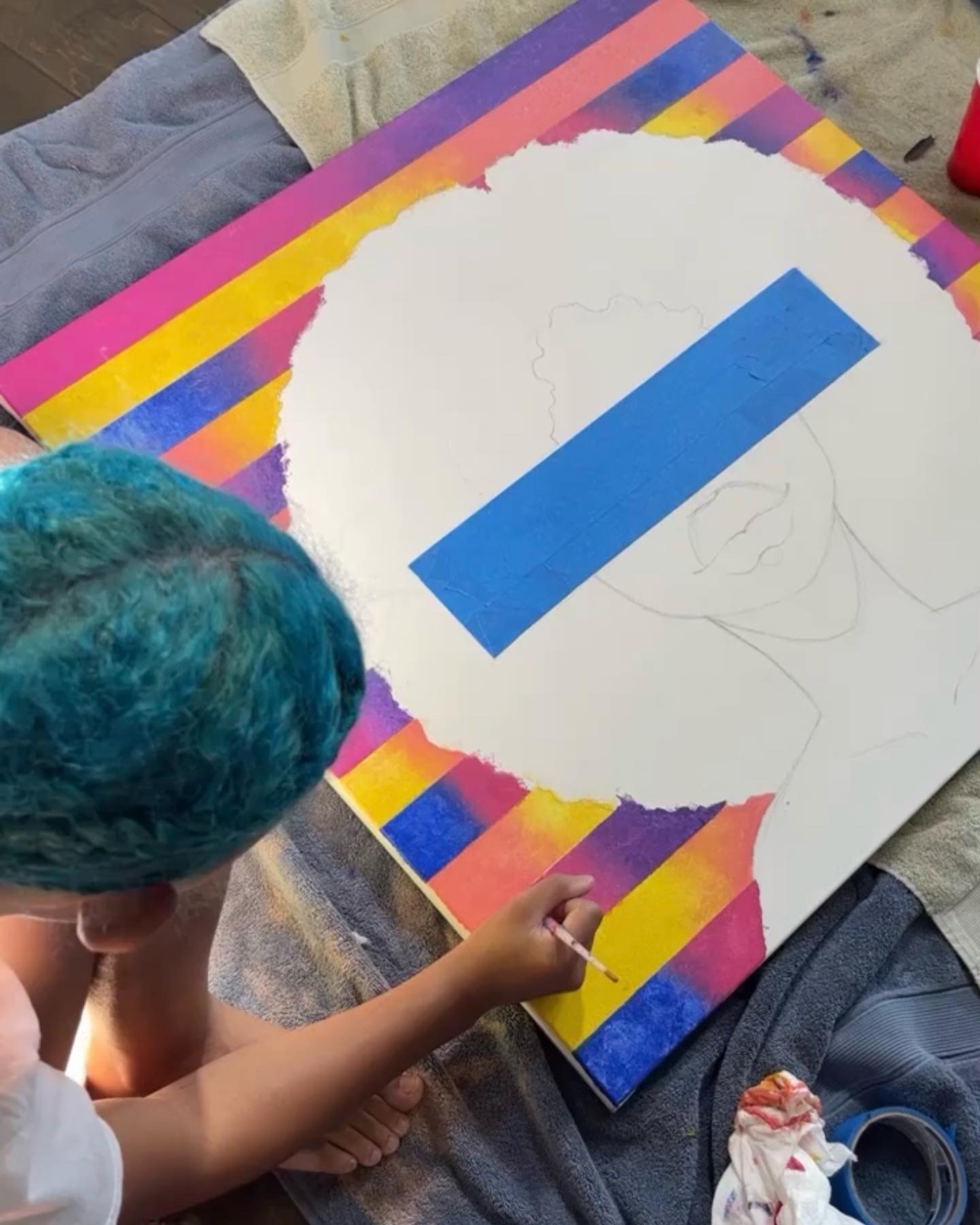 Child with blue-green hair drawing on a colorful striped canvas, which has a large white circle and a blue rectangle.