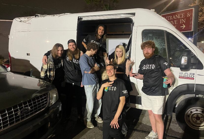 Group of nine people standing outside a white van at night, some holding drinks, posing for a photo.