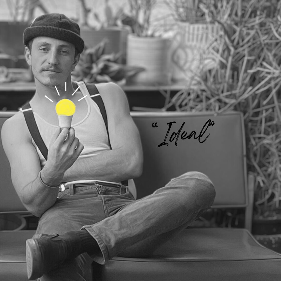 Man sitting cross-legged holding a glowing light bulb, with a sign reading 'Ideal' behind him, in black and white.