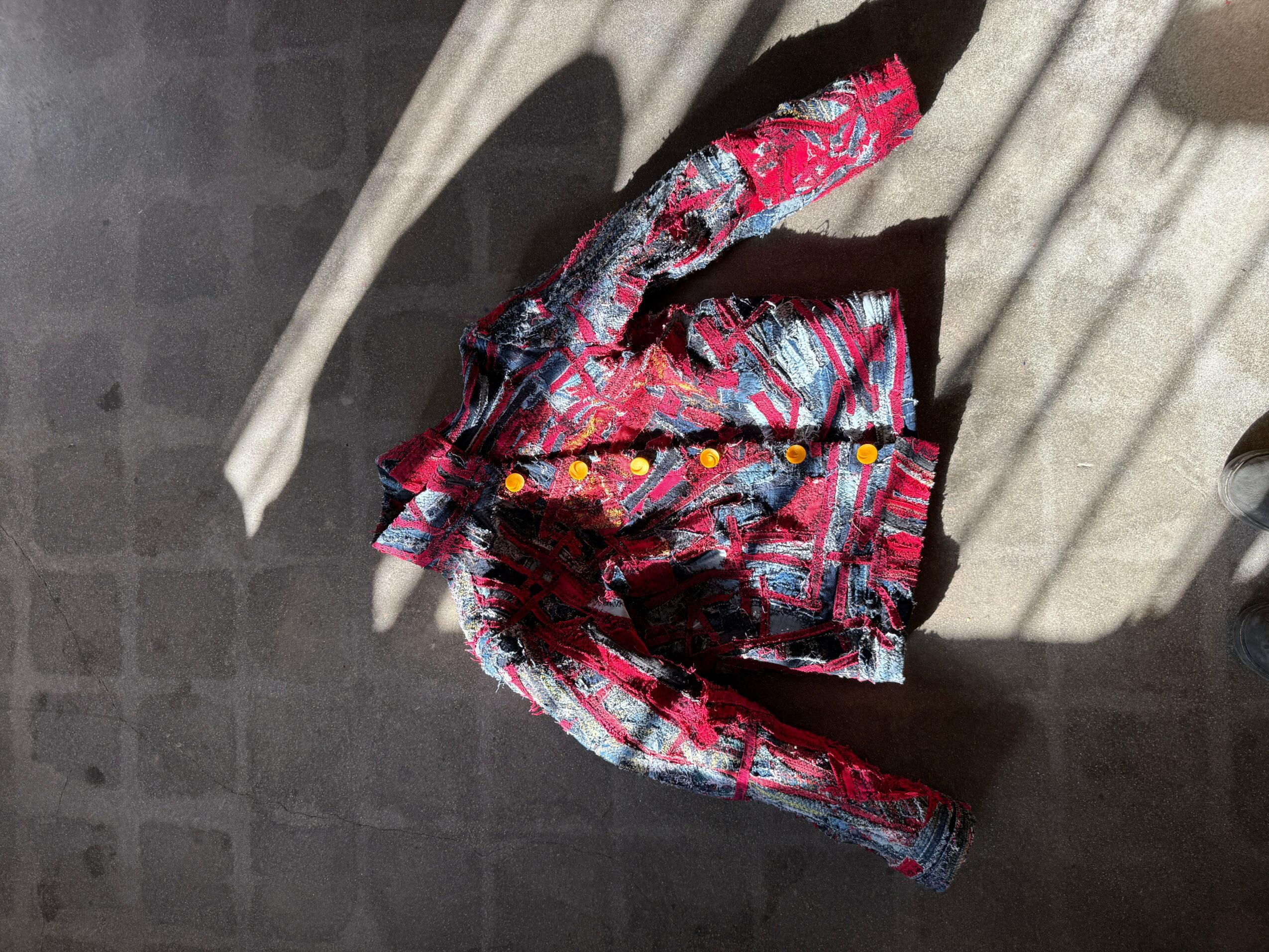 Colorful patterned fabric with red, pink, and black, draped on a surface, with shadows and light patterns.