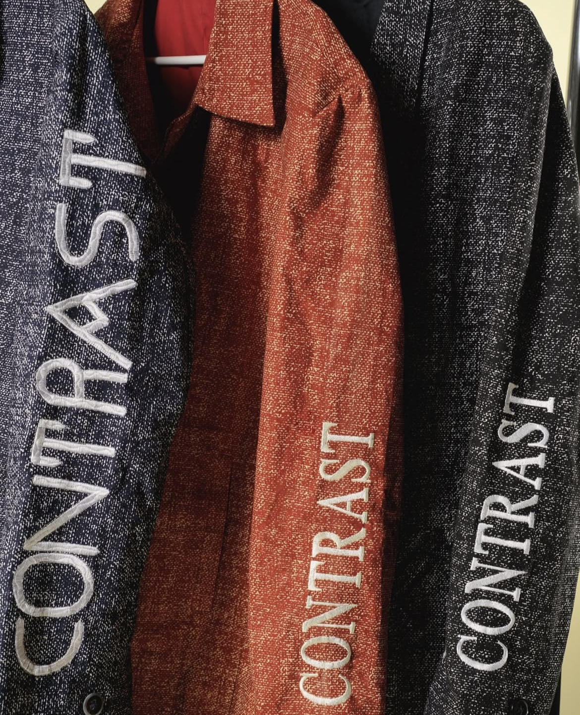 Three jackets hanging, with the middle one rotated 90 degrees, displaying the word 'CONTRAST' vertically on each jacket.
