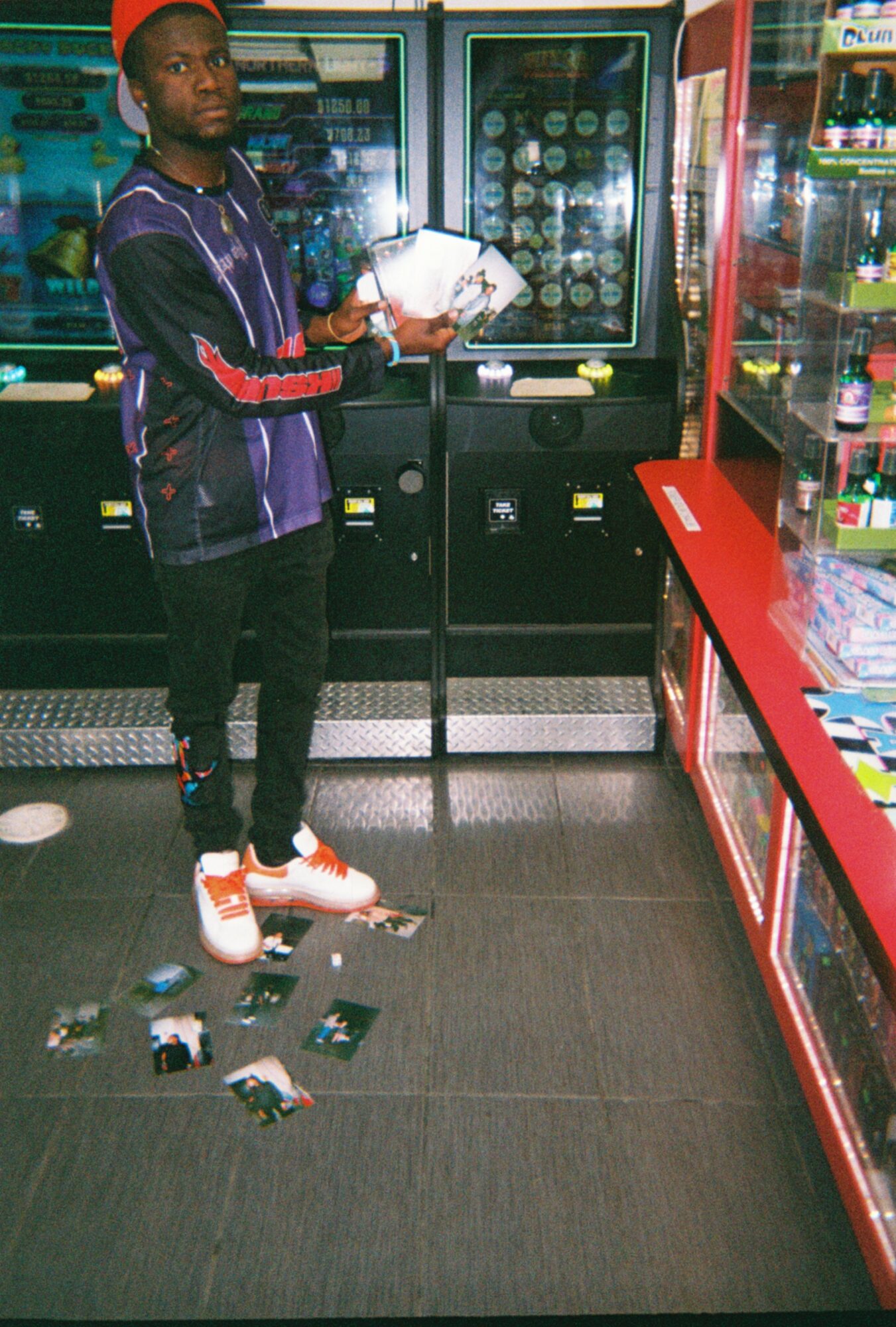 Young person in a store holding a snack, with items on the floor and shelves around, facing left.