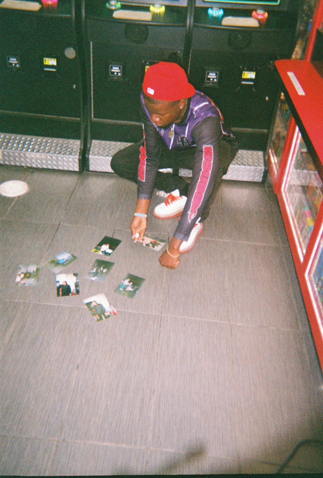 Child in red cap and dark jacket picks up items from the floor in a store, with vending machines behind.